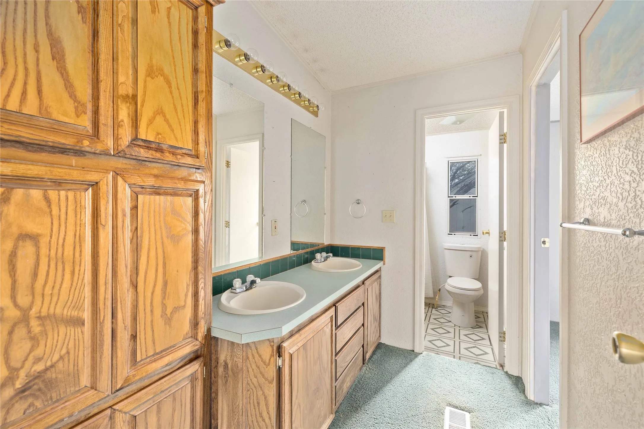 Full bathroom featuring double vanity, a textured ceiling, and light colored carpet