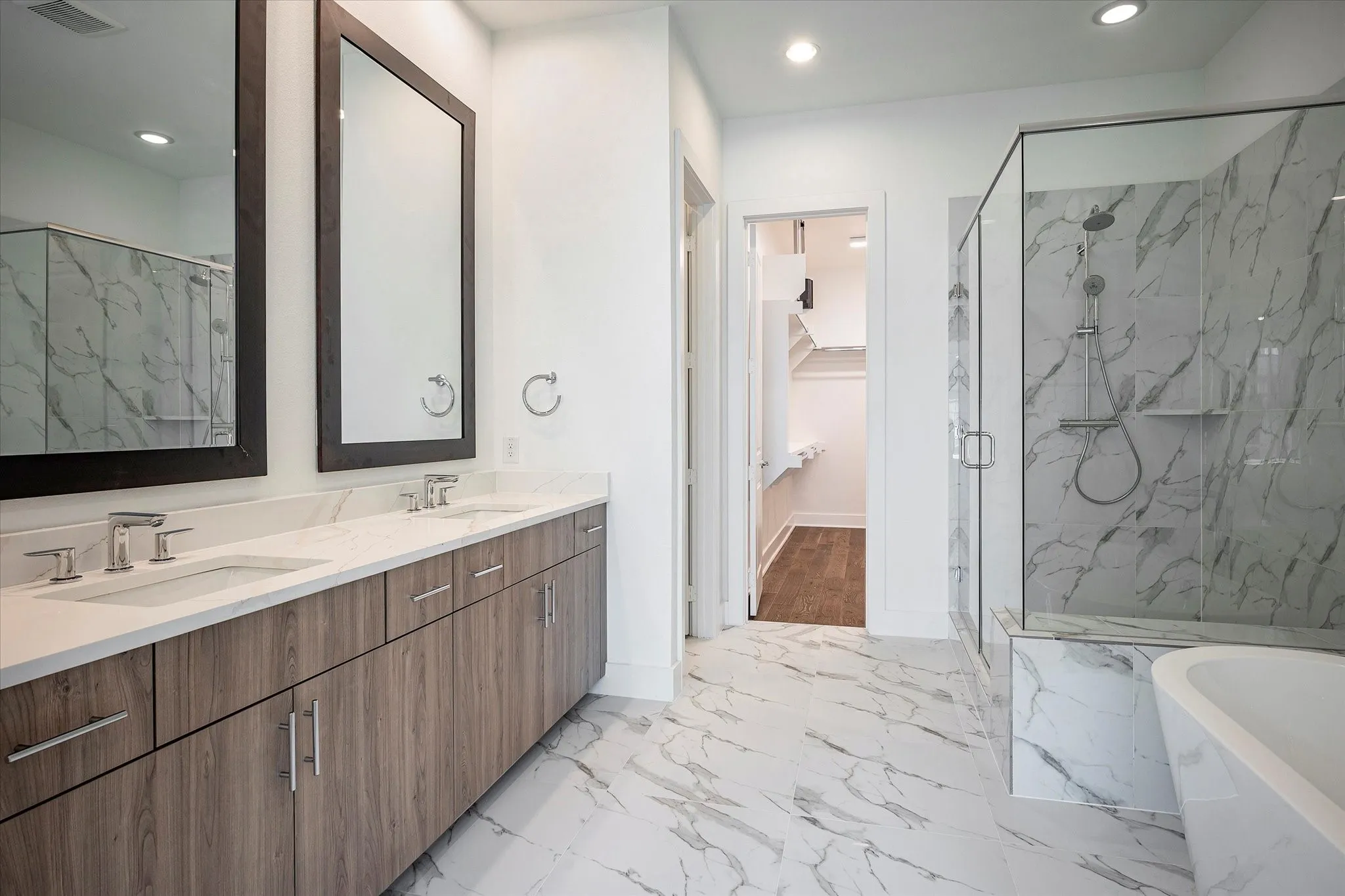 Bathroom with a walk in closet, light marble finish floors, double vanity, a freestanding bath, and recessed lighting