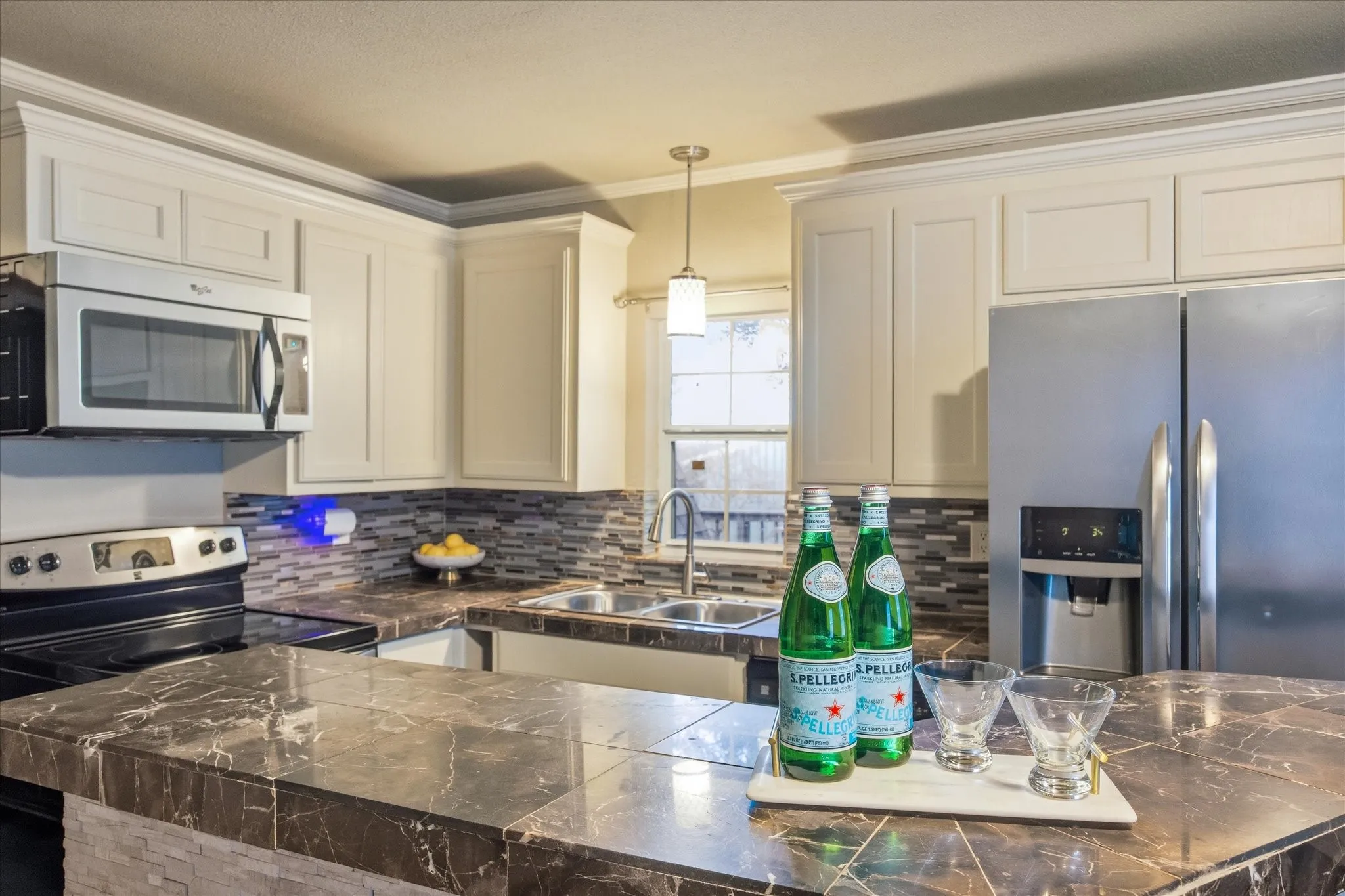 Kitchen featuring appliances with stainless steel finishes, crown molding, hanging light fixtures, backsplash and tile counters