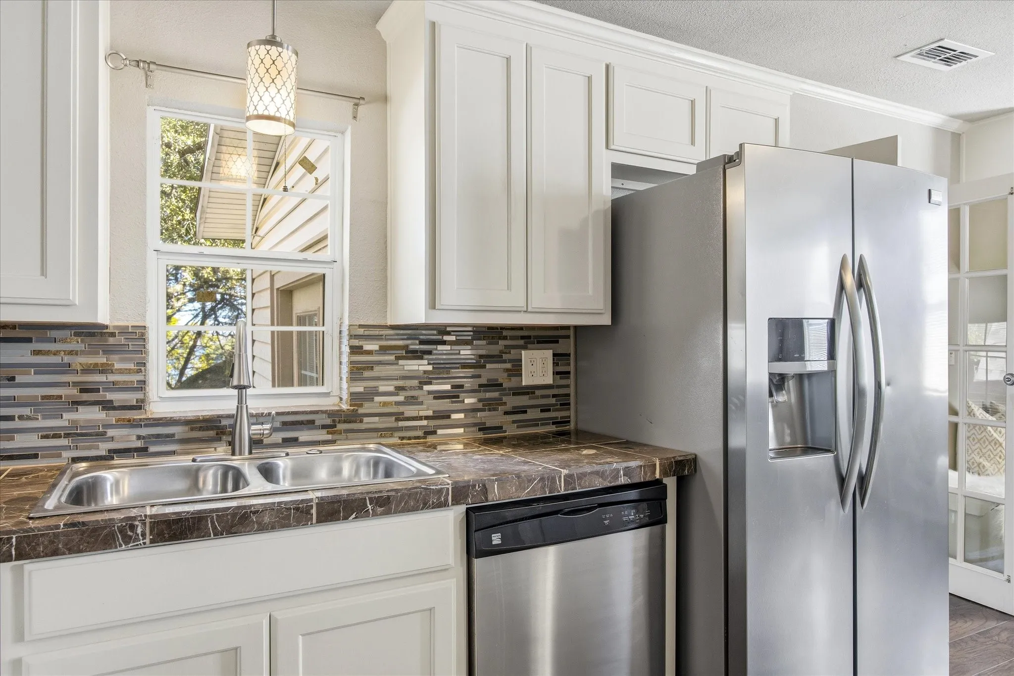 Kitchen with white cabinetry, appliances with stainless steel finishes, tile counters, hanging light fixtures and a textured ceiling