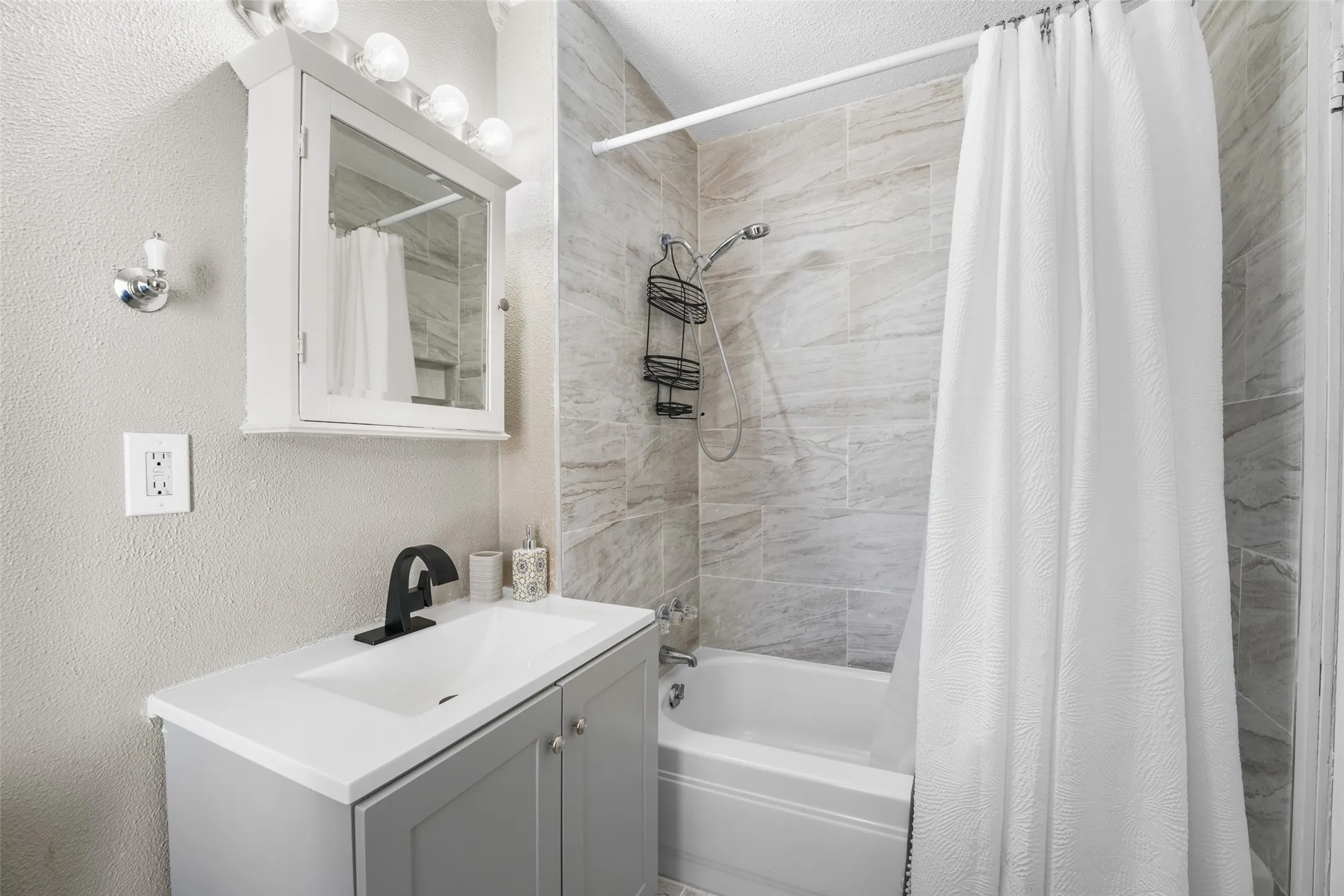 Bathroom with shower / bathtub combination with curtain, a textured wall, and vanity