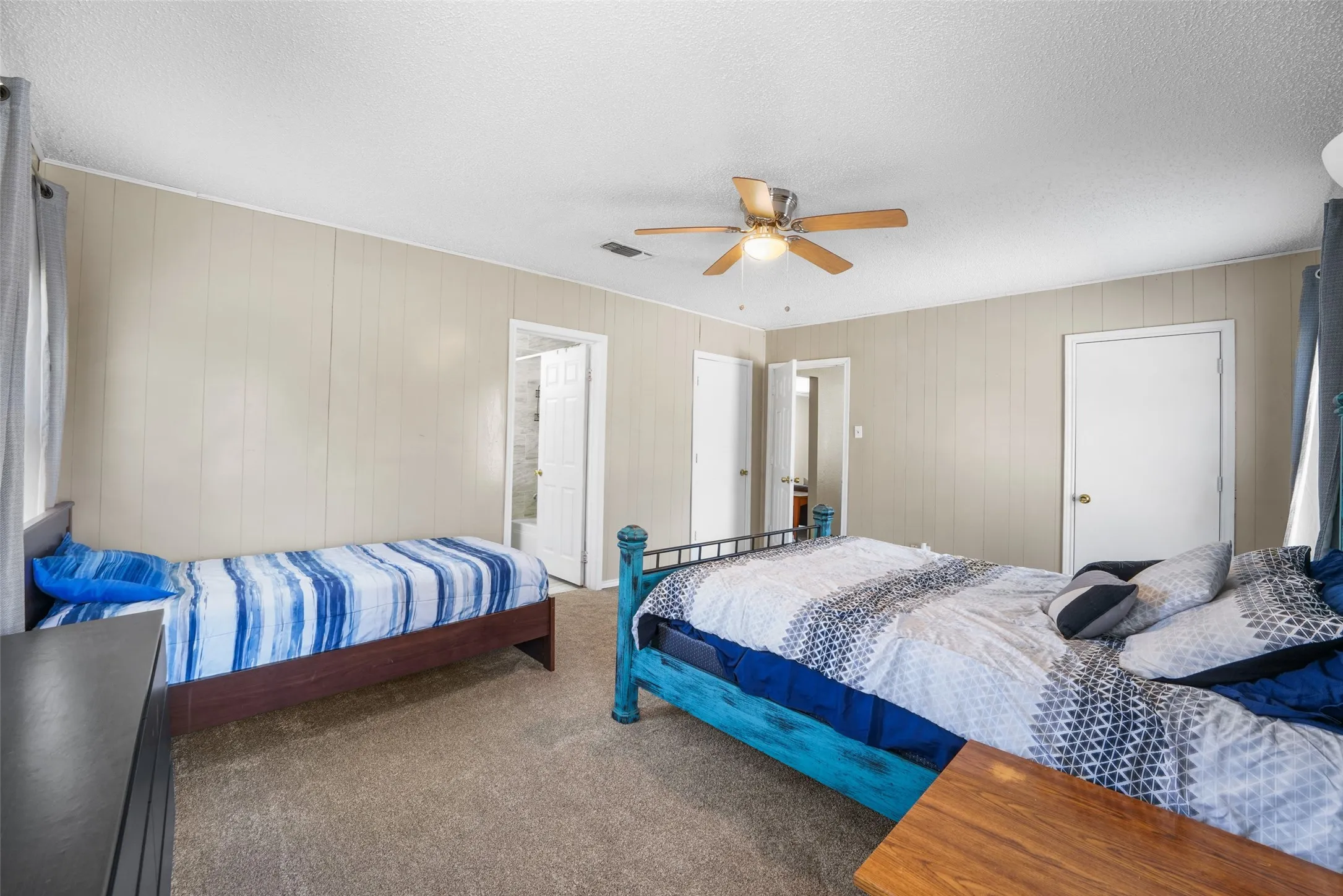 Bedroom featuring carpet, a ceiling fan, a textured ceiling, and wood walls