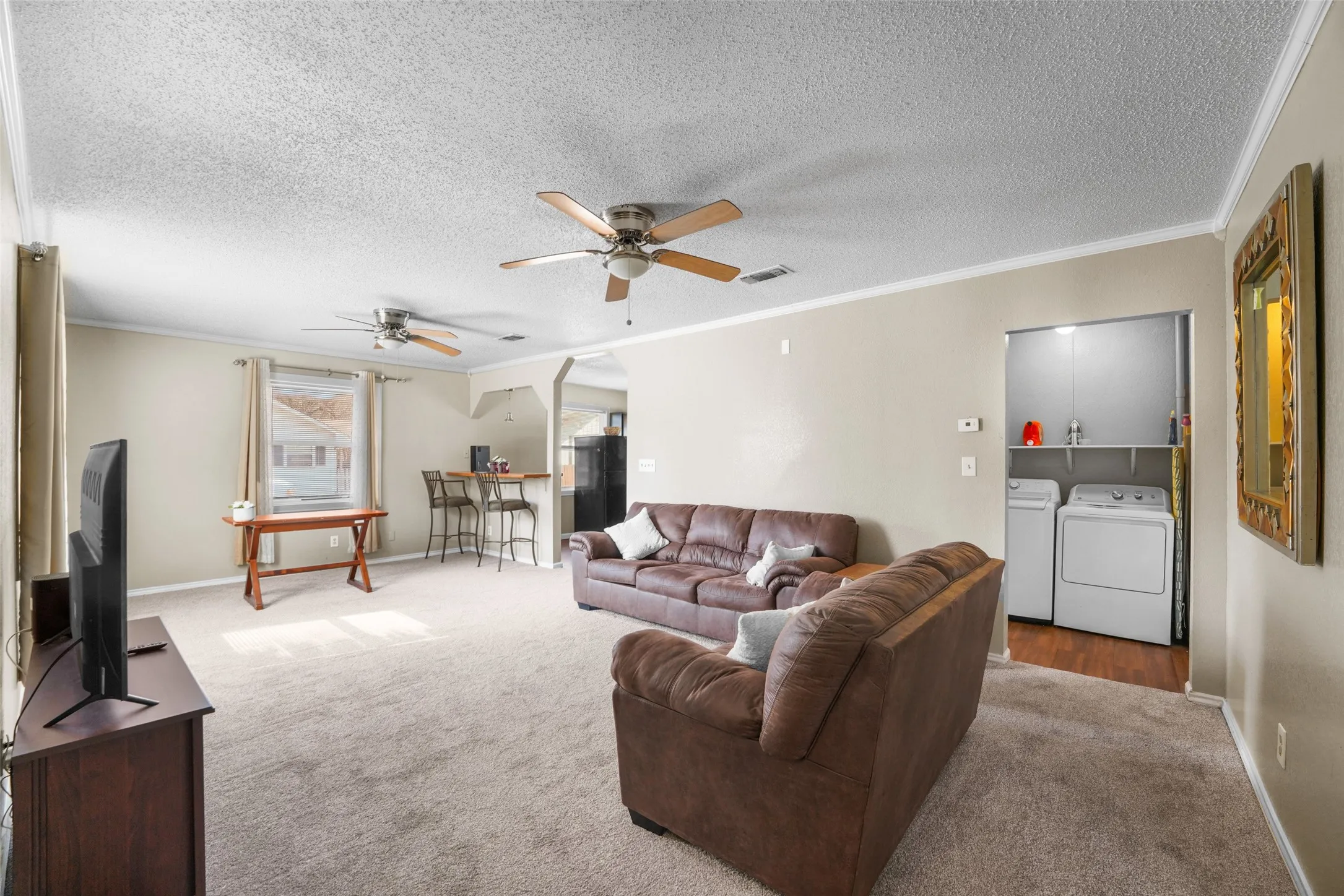 Carpeted living area featuring crown molding, a textured ceiling, washing machine and dryer, arched walkways, and a ceiling fan
