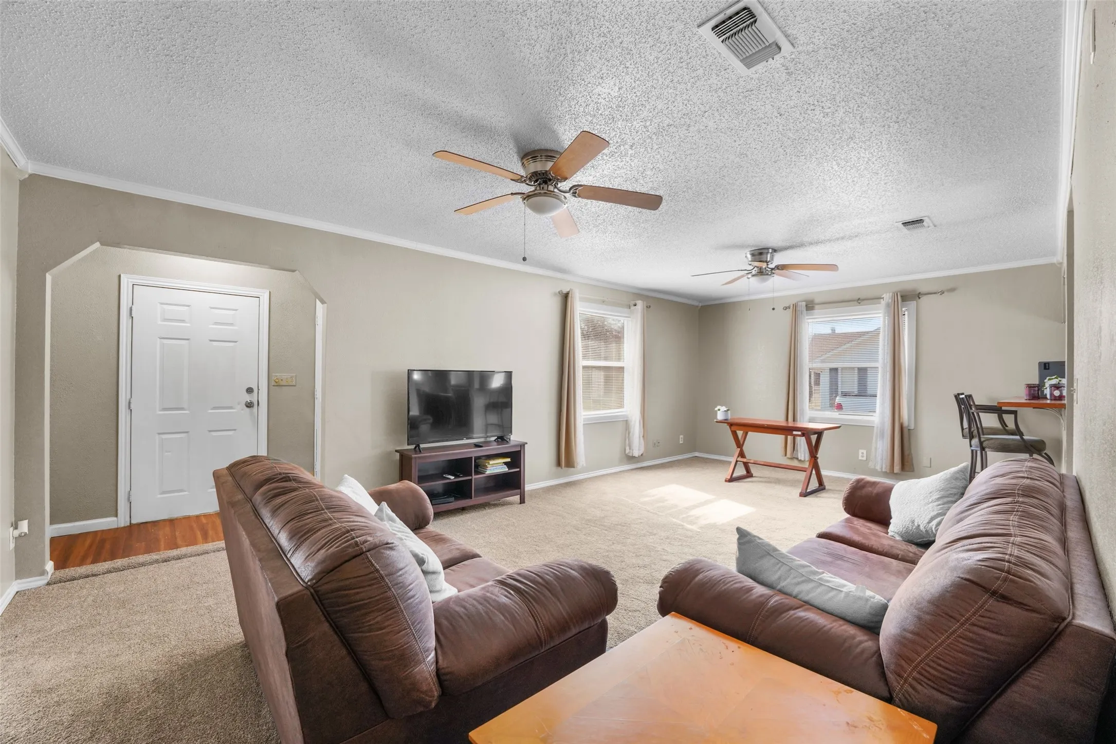 Carpeted living area featuring ornamental molding, a textured ceiling, and ceiling fan