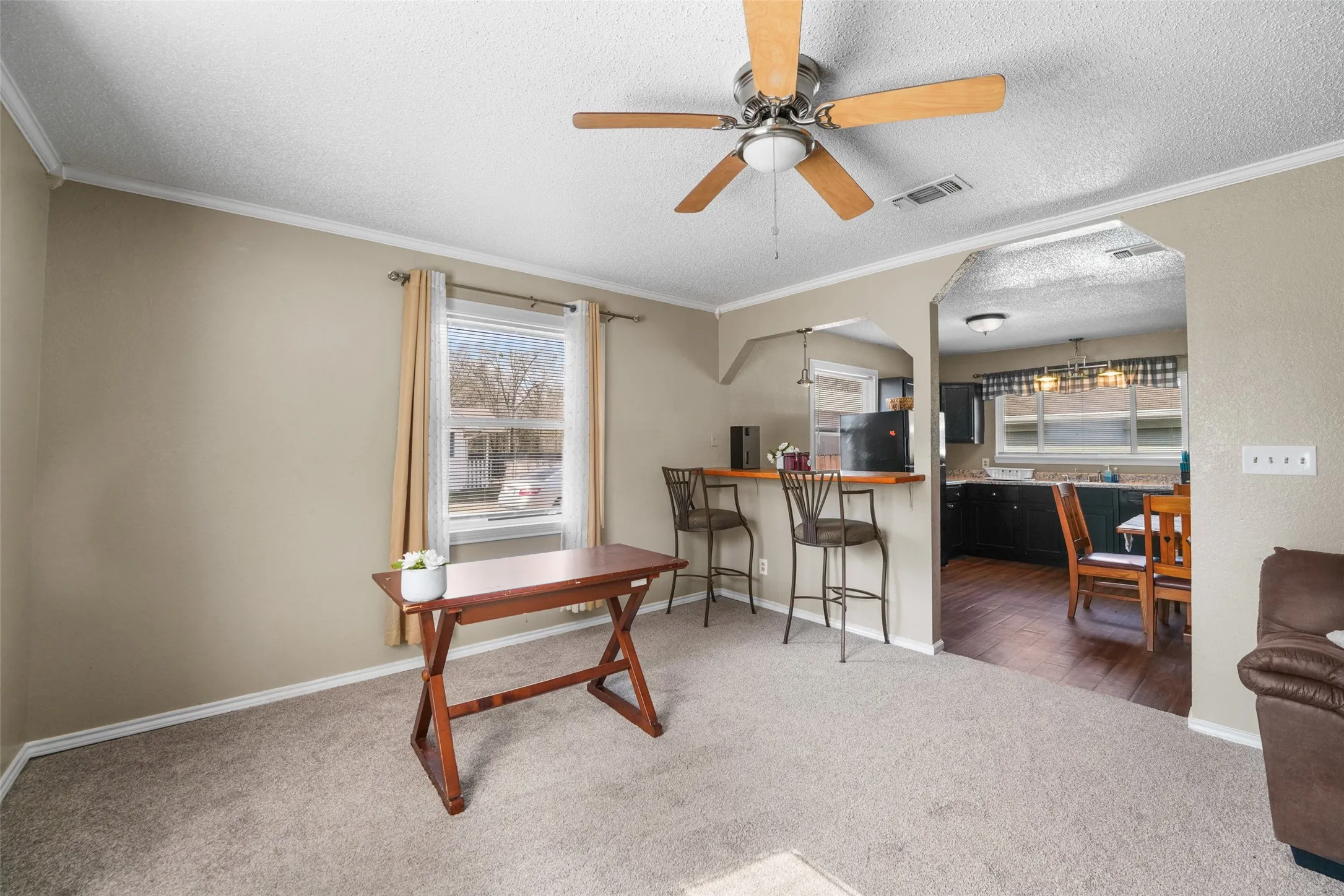 Office area featuring crown molding, a textured ceiling, a ceiling fan, carpet flooring, and arched walkways