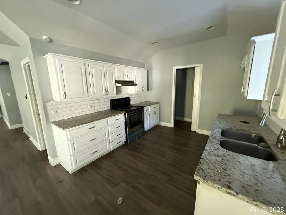 Kitchen with light stone counters, stainless steel electric stove, white cabinets, tasteful backsplash, and vaulted ceiling