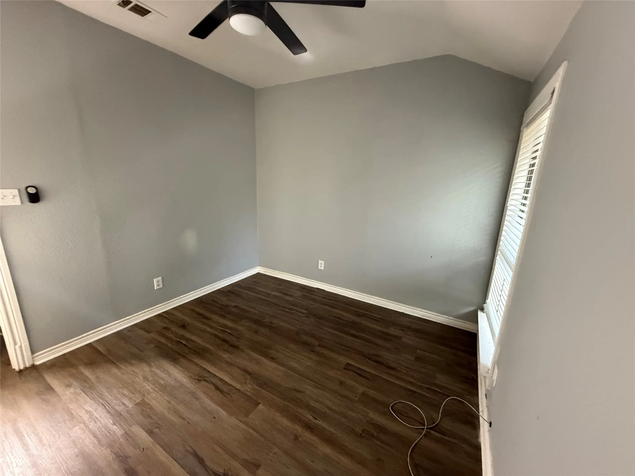 Empty room featuring dark wood-style flooring, vaulted ceiling, and ceiling fan