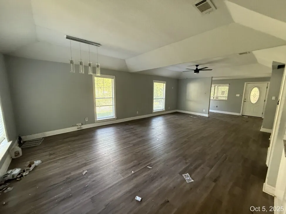 Unfurnished living room featuring dark wood-type flooring, a ceiling fan, and lofted ceiling