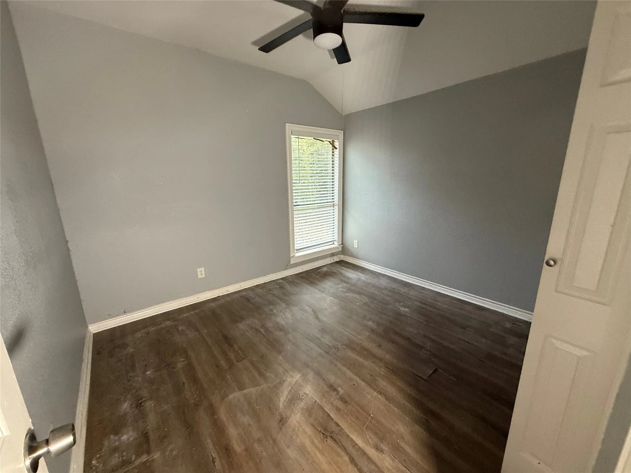 Empty room featuring vaulted ceiling, dark wood finished floors, and a ceiling fan