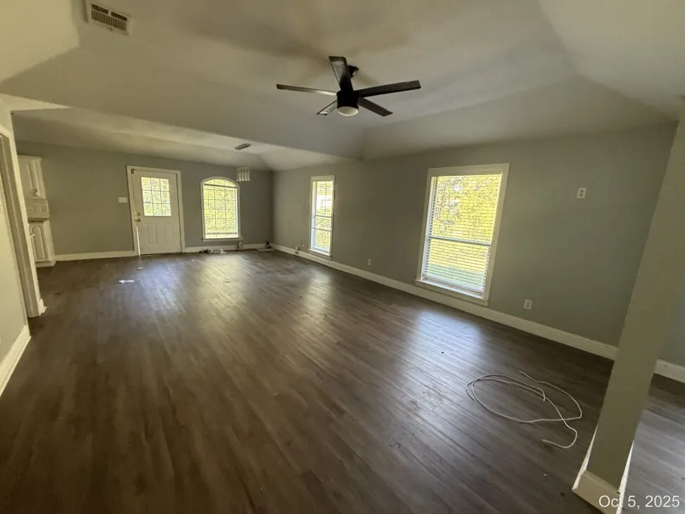 Unfurnished living room featuring dark wood-type flooring, plenty of natural light, and ceiling fan