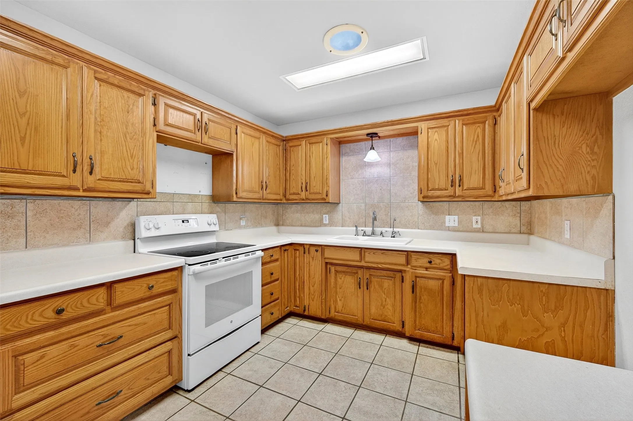 Kitchen with white range with electric cooktop, light countertops, brown cabinets, light tile patterned floors, and tasteful backsplash