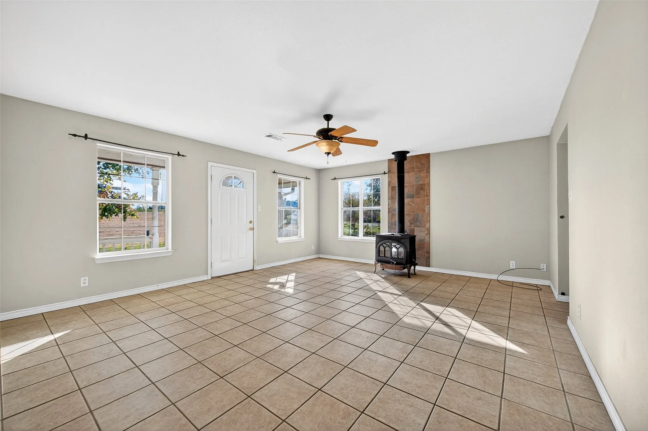 Unfurnished living room featuring a wood stove, a ceiling fan, and light tile patterned floors
