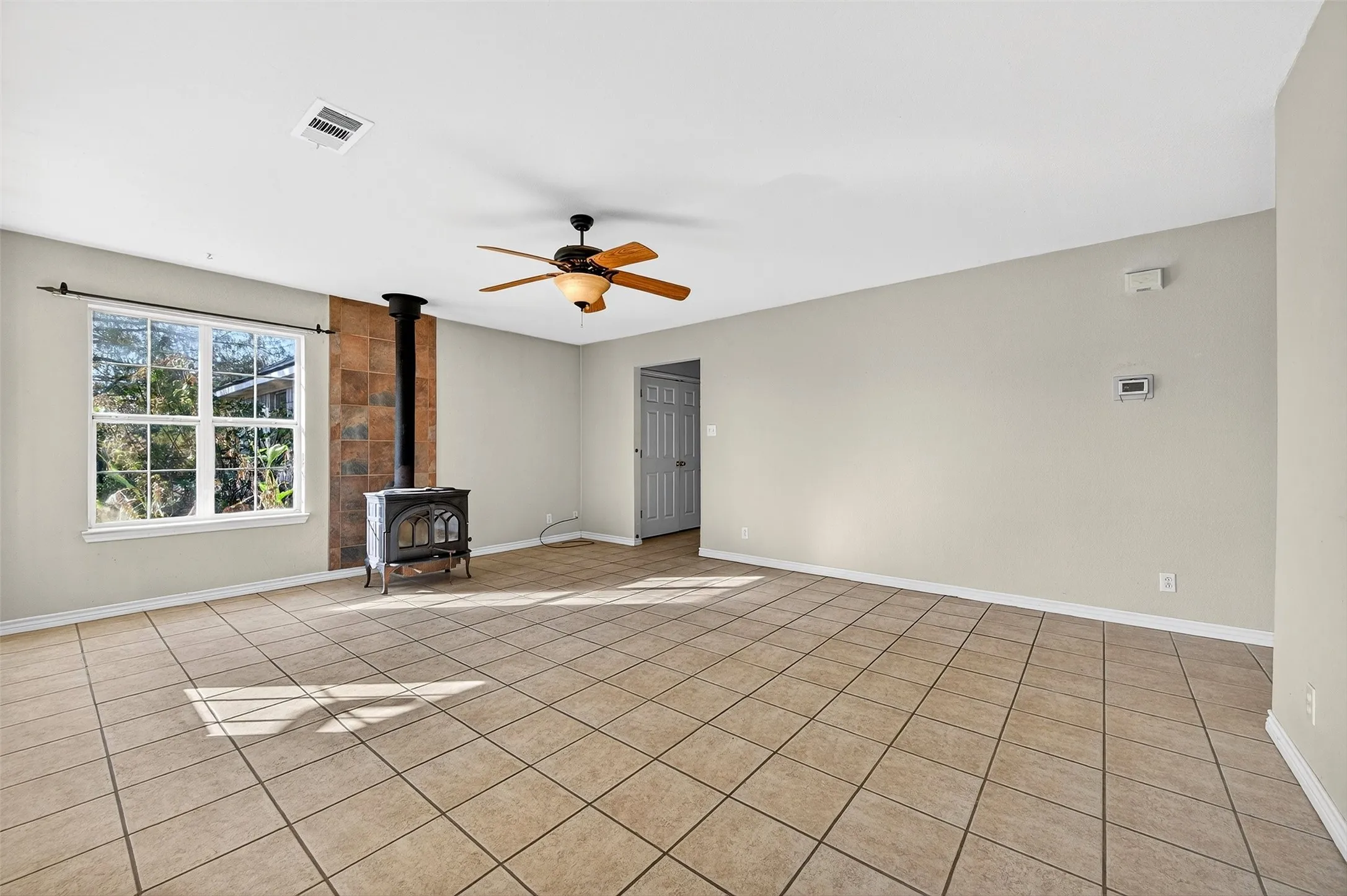 Unfurnished living room featuring a wood stove, ceiling fan, and light tile patterned floors