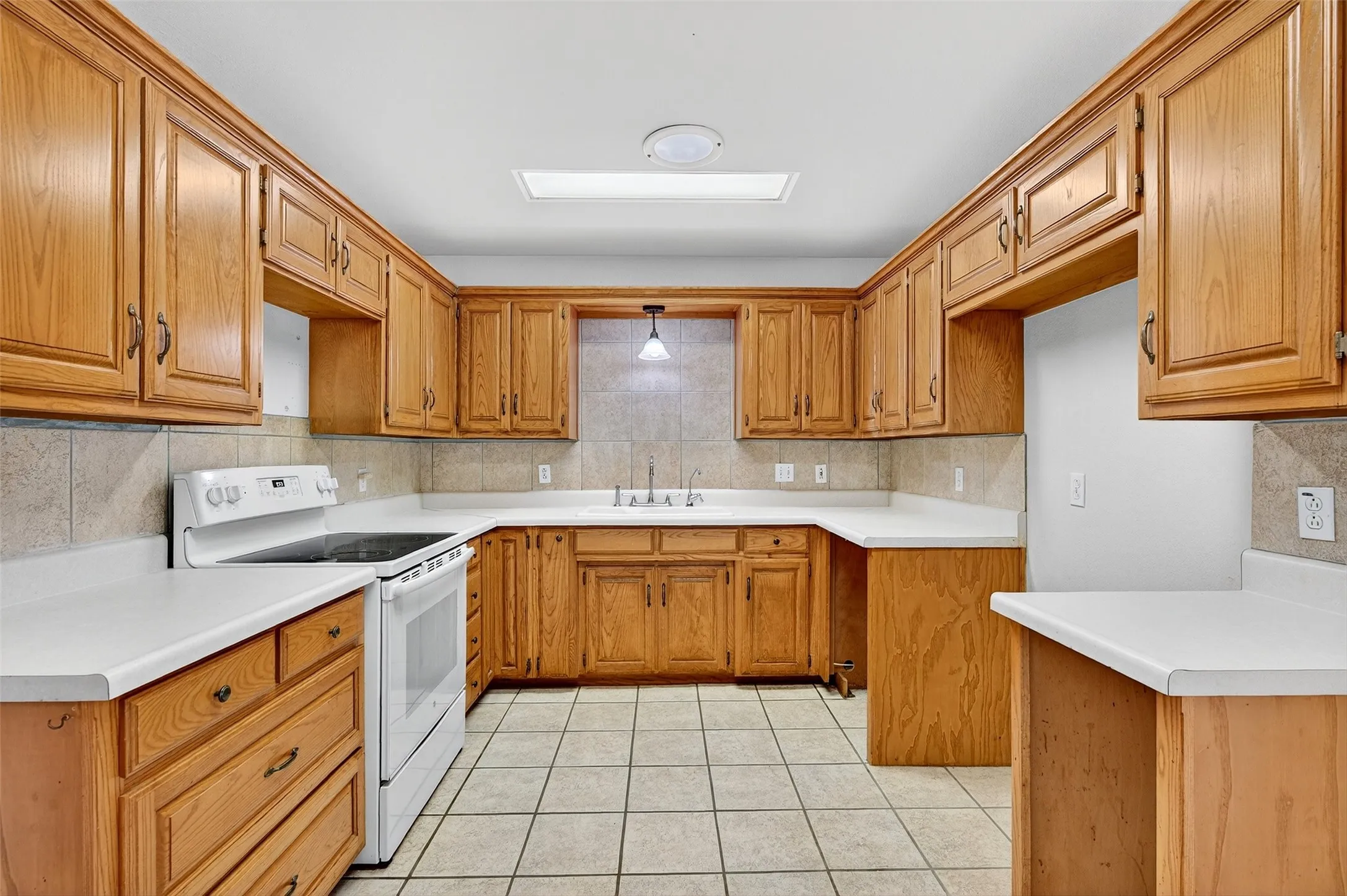 Kitchen featuring white electric range, brown cabinets, decorative backsplash, light countertops, and light tile patterned floors