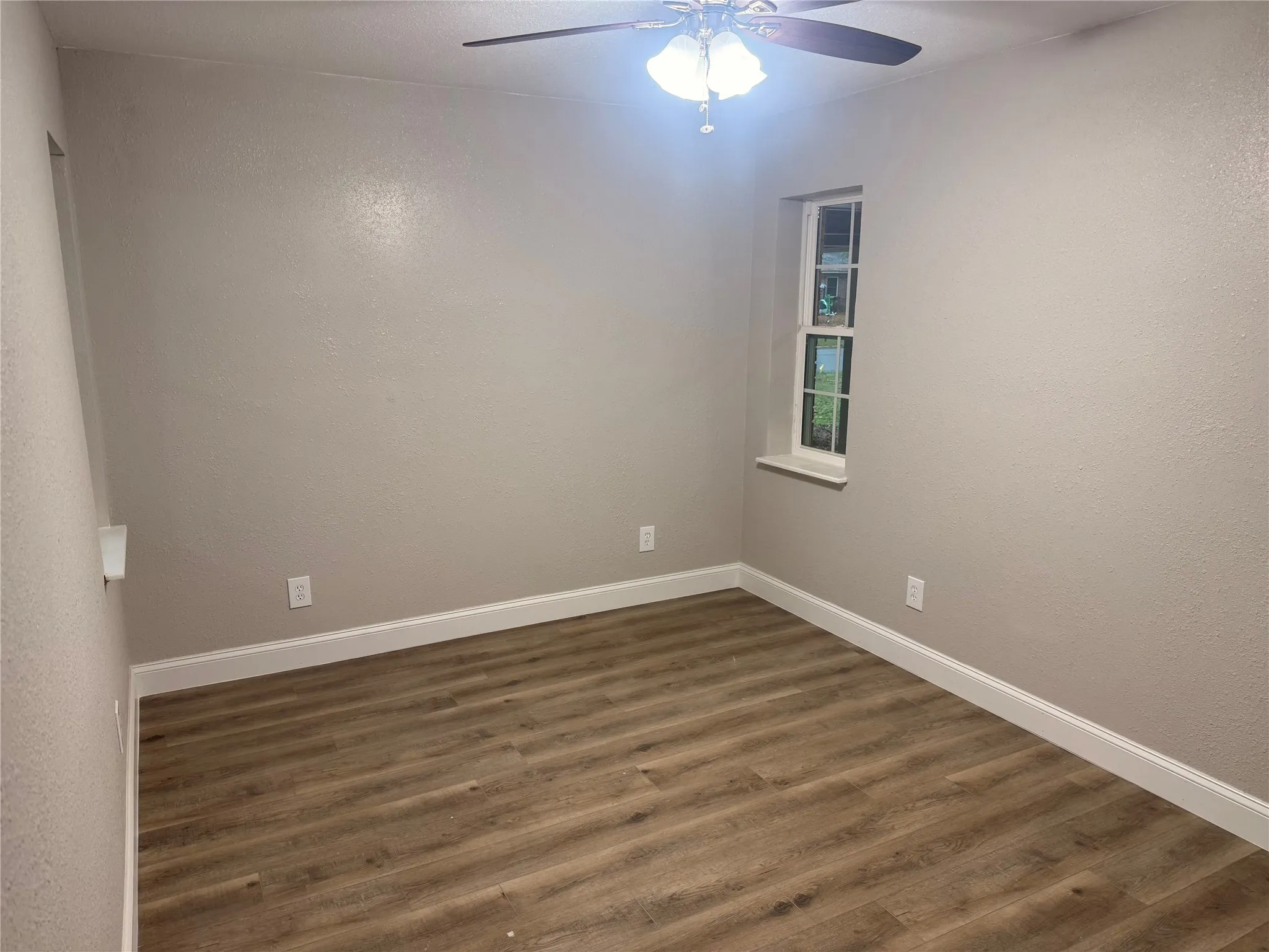 Unfurnished room with dark wood finished floors, a textured wall, and a ceiling fan