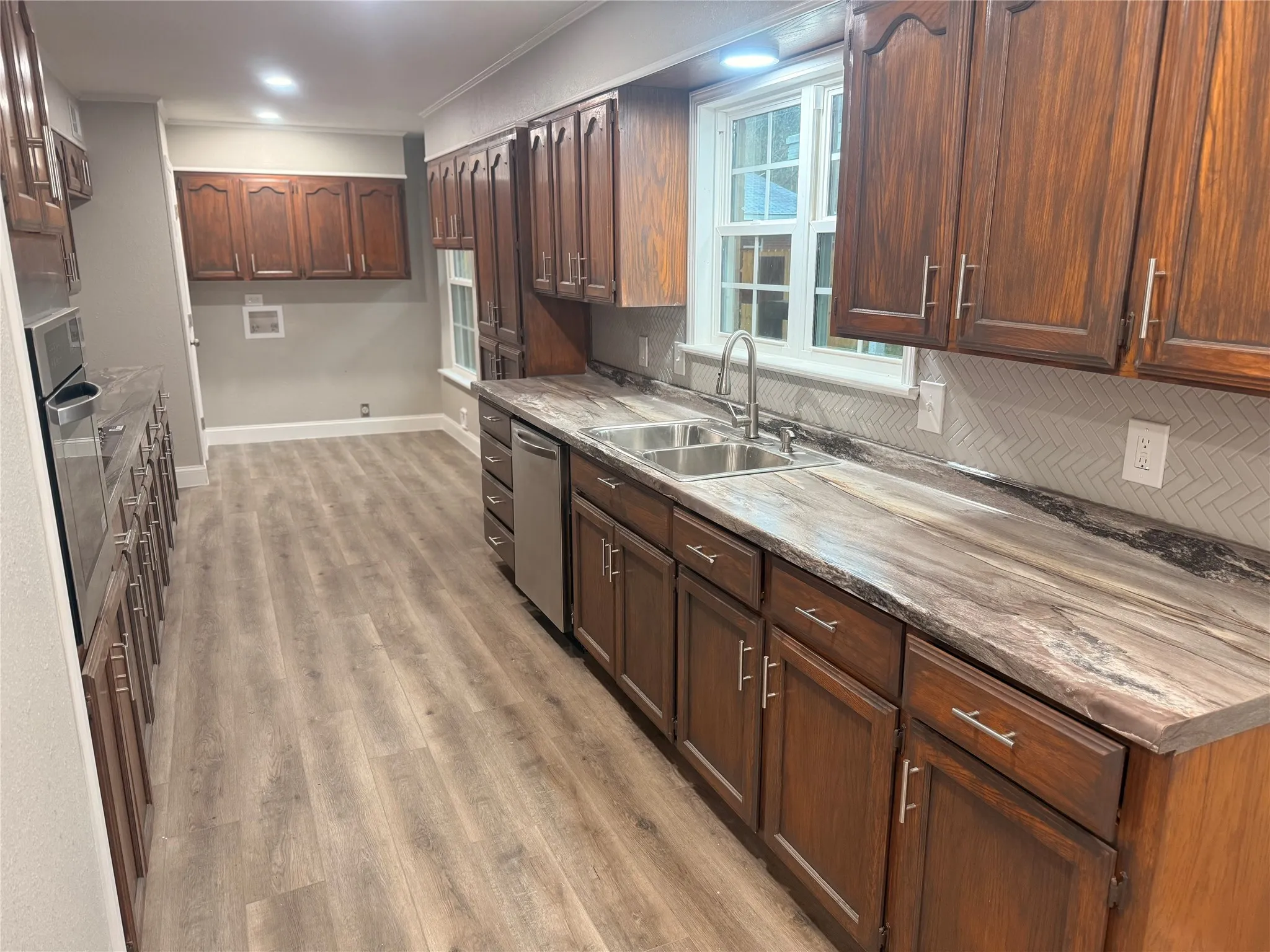 Kitchen featuring light wood-style flooring, ornamental molding, stainless steel appliances, backsplash, and dark brown cabinets