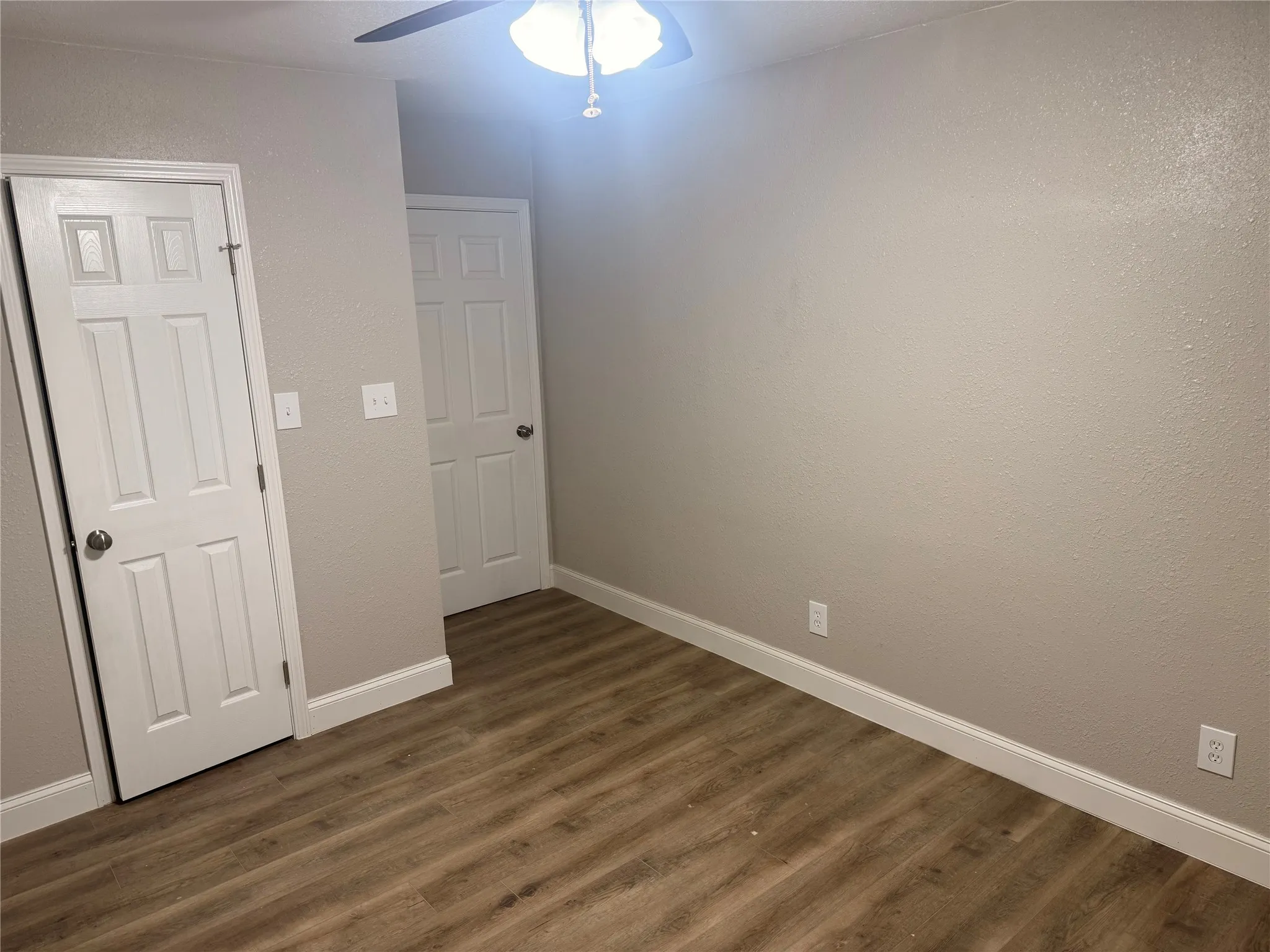 Unfurnished room with dark wood-style floors, a textured wall, and ceiling fan
