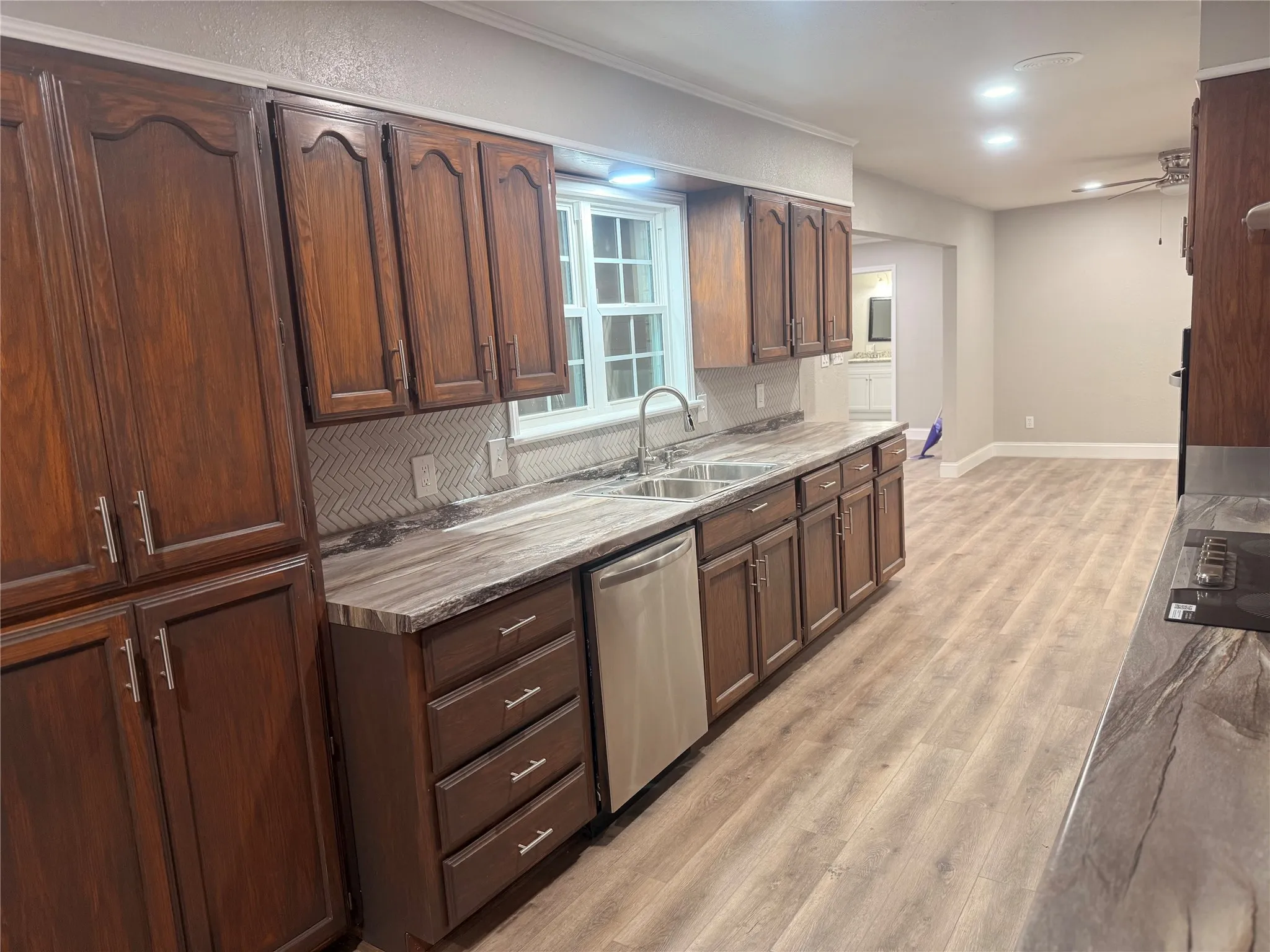 Kitchen featuring light wood-style floors, dishwasher, backsplash, light countertops, and black electric cooktop