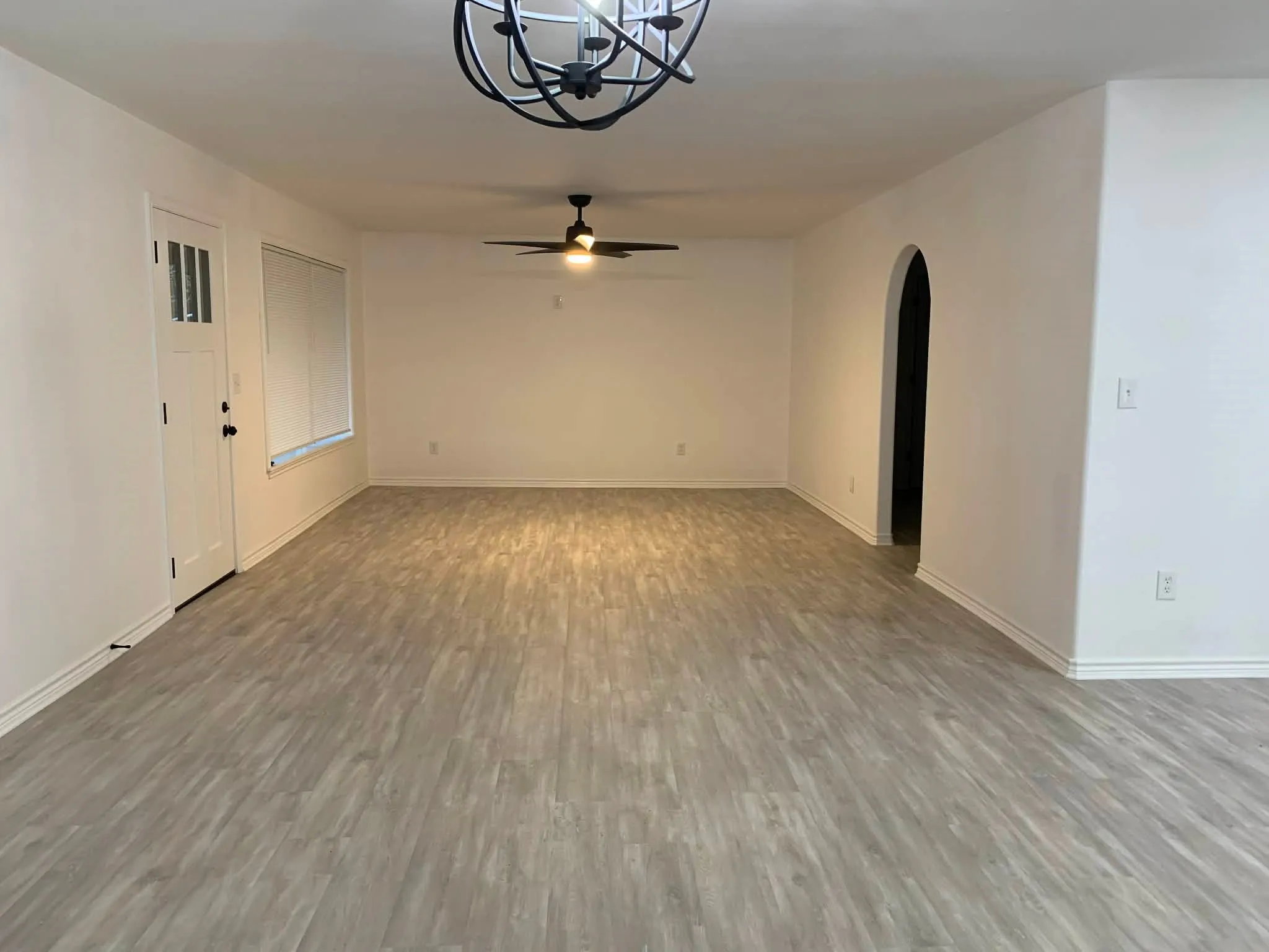 Empty room with arched walkways, wood finished floors, a chandelier, and a ceiling fan