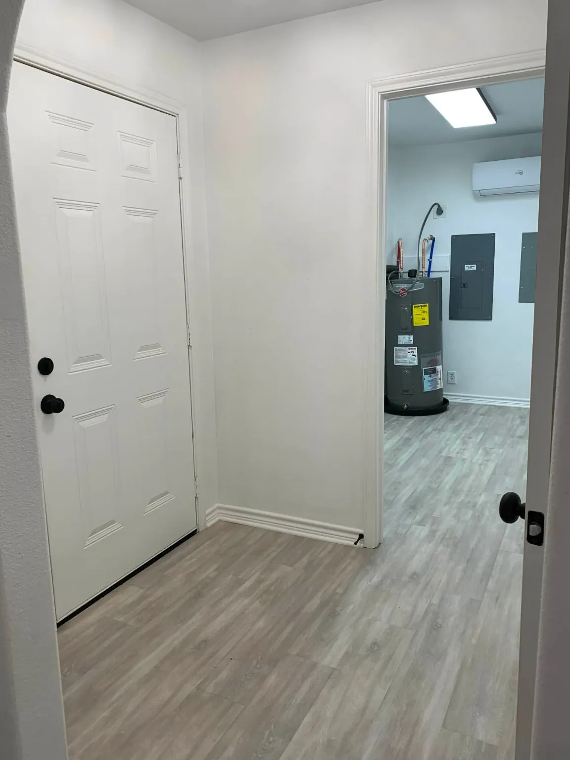 Hallway featuring light wood-style floors, electric panel, water heater, and a wall unit AC