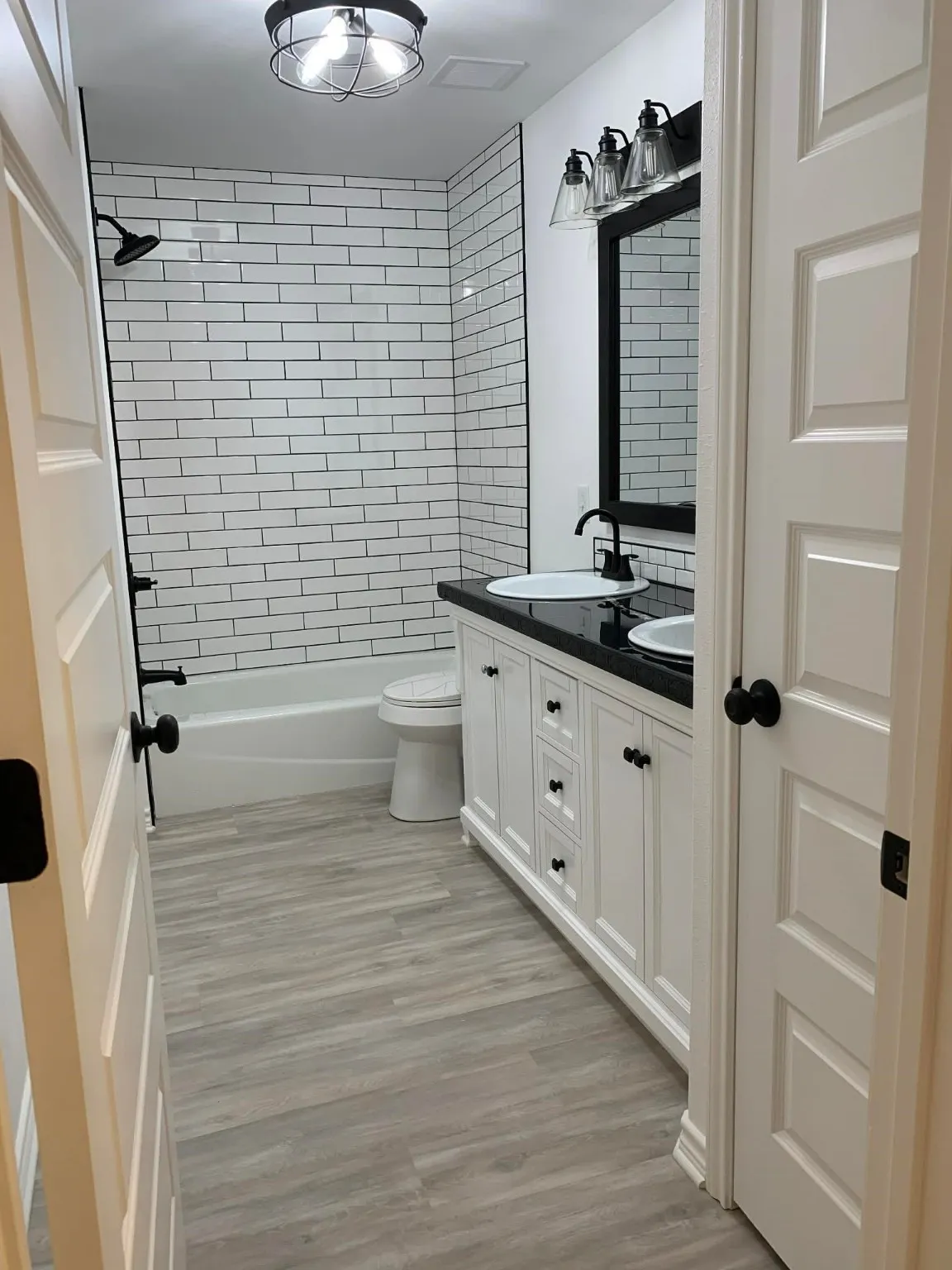 Bathroom with double vanity, shower / washtub combination, and light wood finished floors