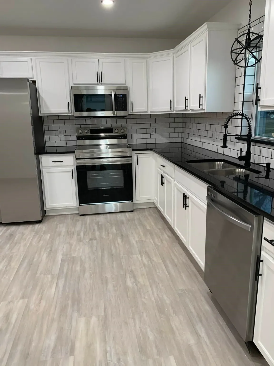 Kitchen with stainless steel appliances, decorative light fixtures, white cabinets, and tasteful backsplash