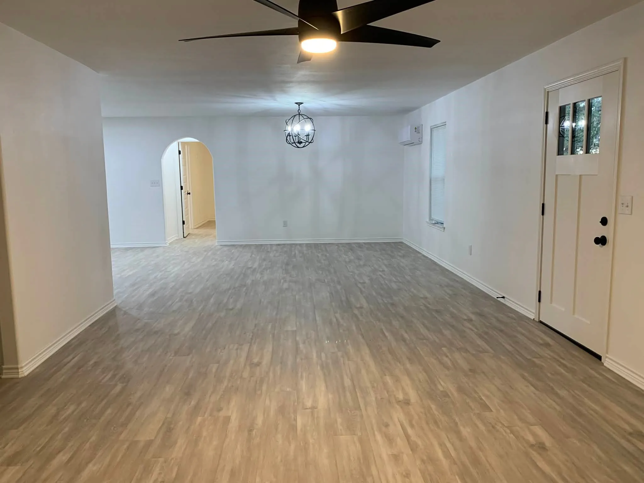 Empty room featuring arched walkways, wood finished floors, a ceiling fan, and a chandelier