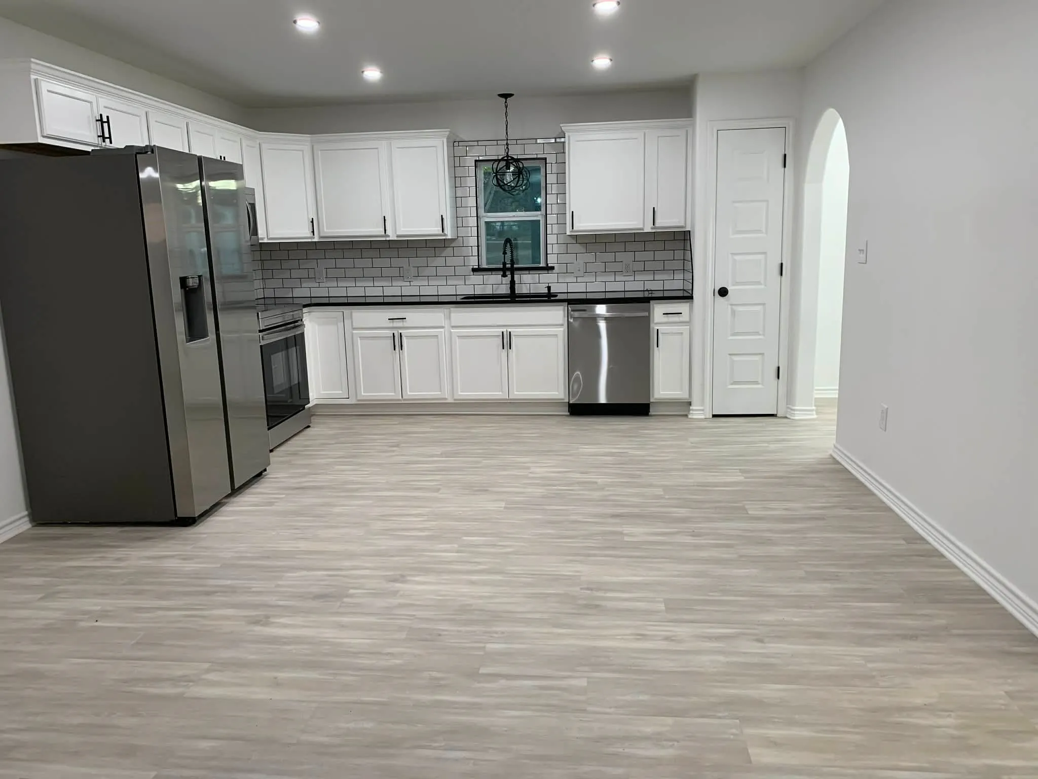 Kitchen featuring stainless steel appliances, dark countertops, white cabinetry, arched walkways, and pendant lighting