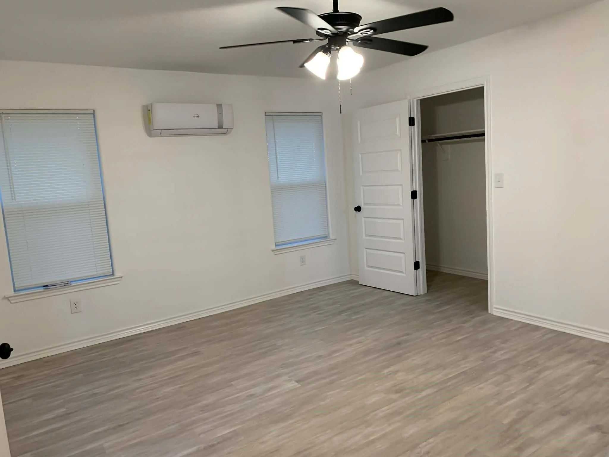 Unfurnished bedroom featuring wood finished floors, a closet, ceiling fan, and a wall mounted air conditioner