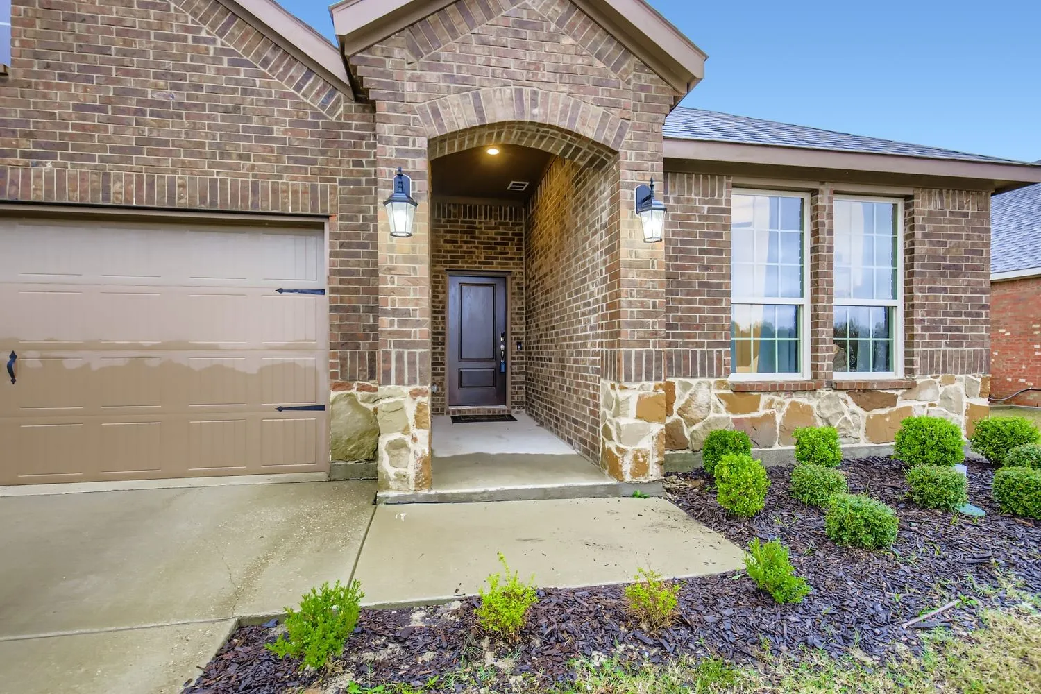 Entrance to property featuring an attached garage, brick siding, and roof with shingles