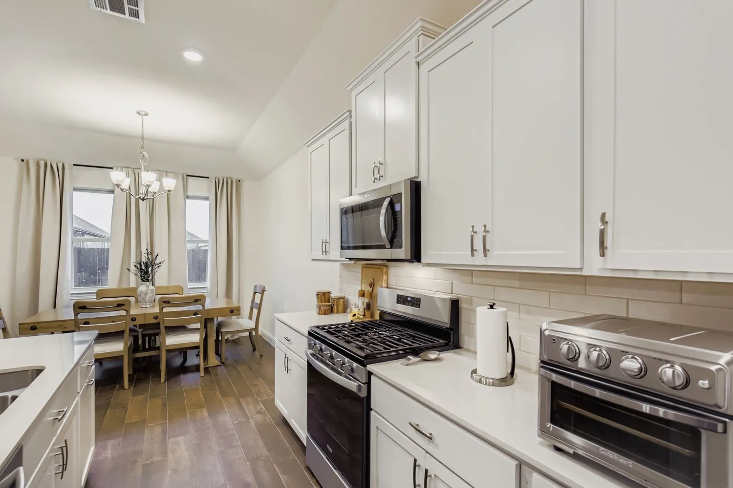 Kitchen featuring stainless steel appliances, decorative backsplash, white cabinetry, dark wood-style flooring, and pendant lighting