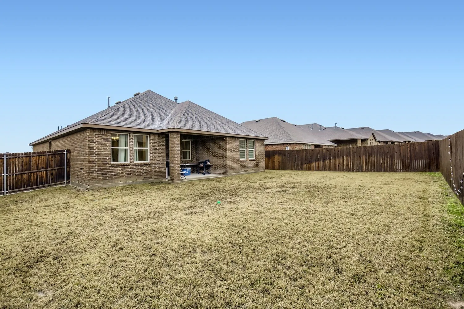 Back of property with a patio, roof with shingles, a fenced backyard, and brick siding