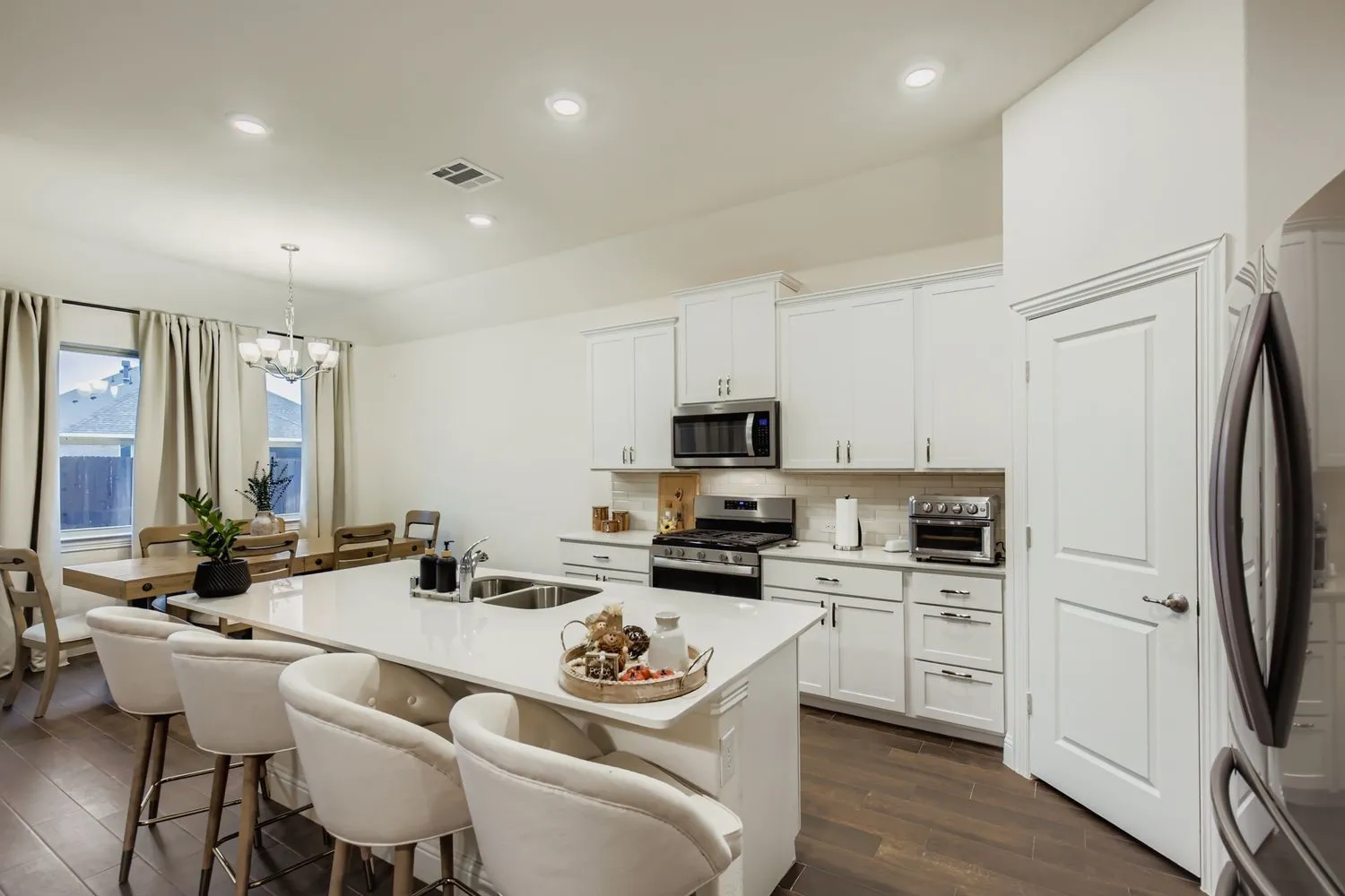 Kitchen featuring appliances with stainless steel finishes, dark wood-type flooring, tasteful backsplash, white cabinetry, and hanging light fixtures