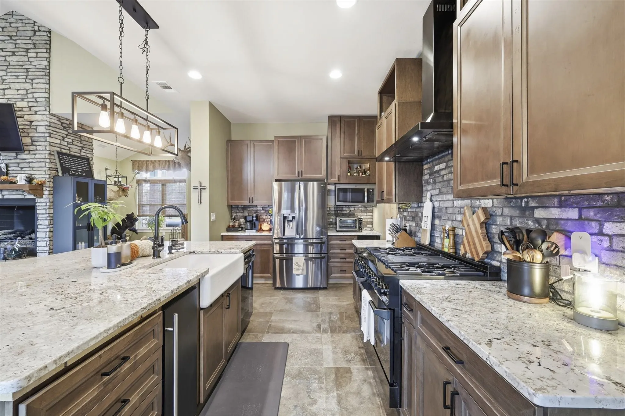 Kitchen featuring stainless steel appliances, wall chimney exhaust hood, pendant lighting, light stone countertops, and tasteful backsplash
