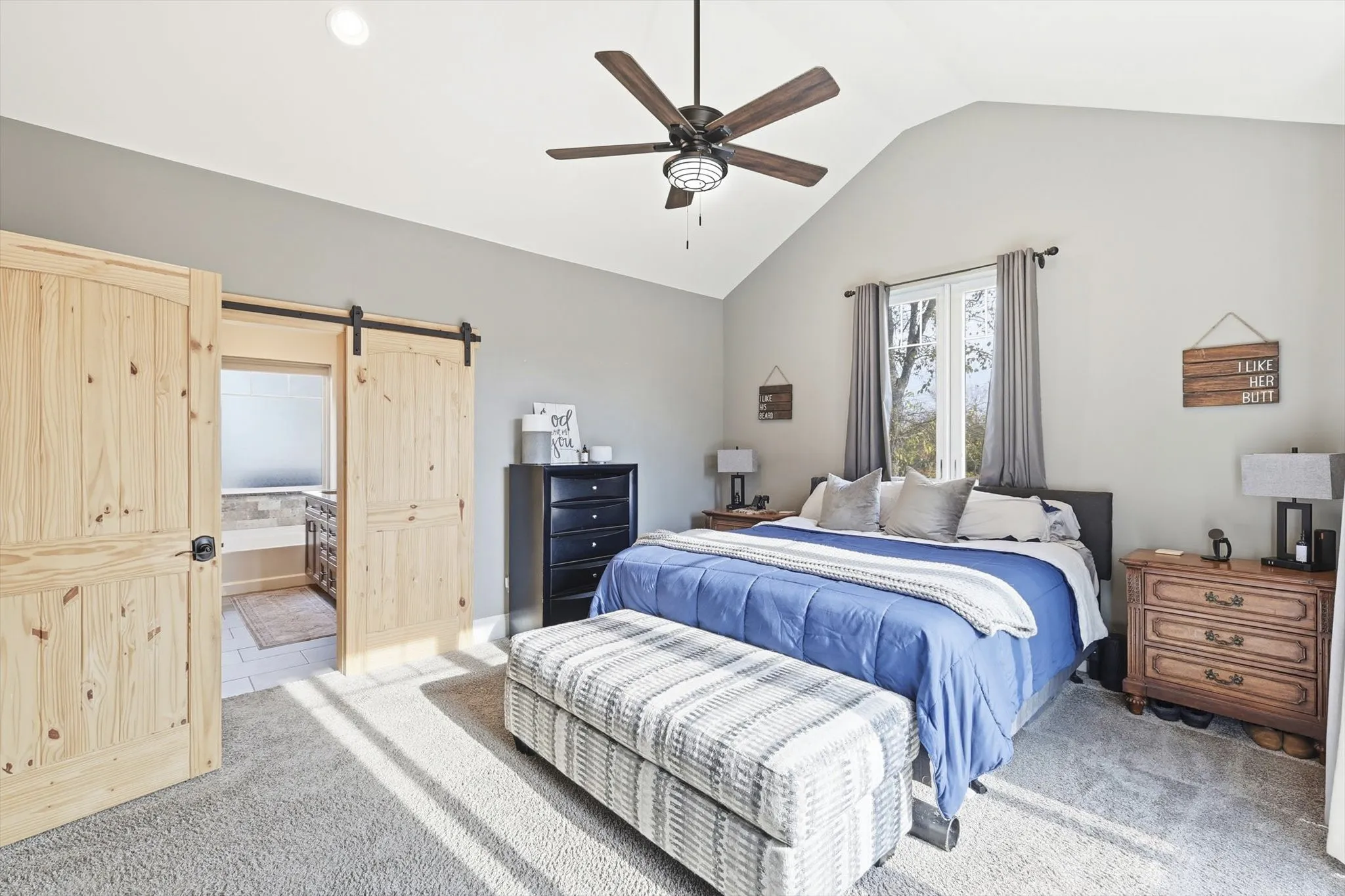 Carpeted bedroom featuring a barn door, lofted ceiling, ceiling fan, and ensuite bathroom