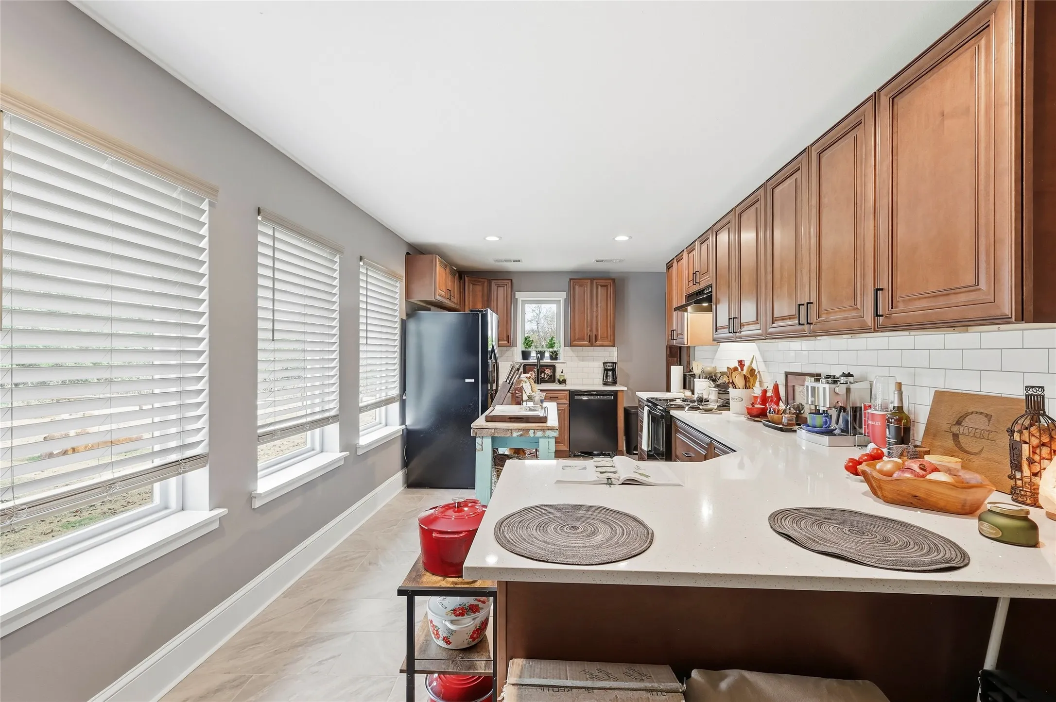 Kitchen featuring a peninsula, black appliances, decorative backsplash, brown cabinetry, and a breakfast bar