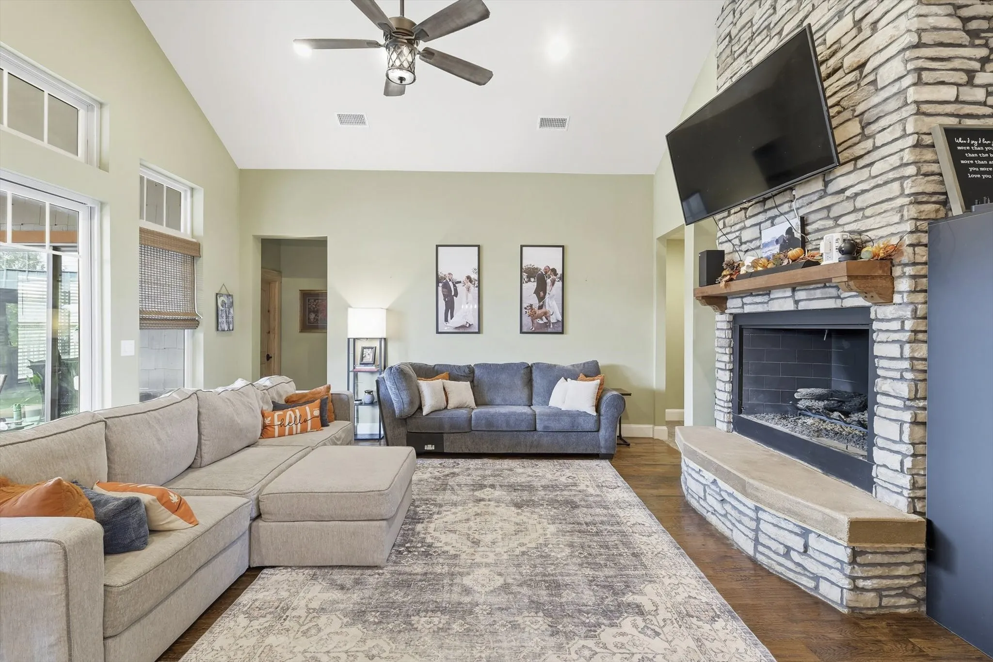 Living room featuring dark wood finished floors, a fireplace, high vaulted ceiling, and a ceiling fan