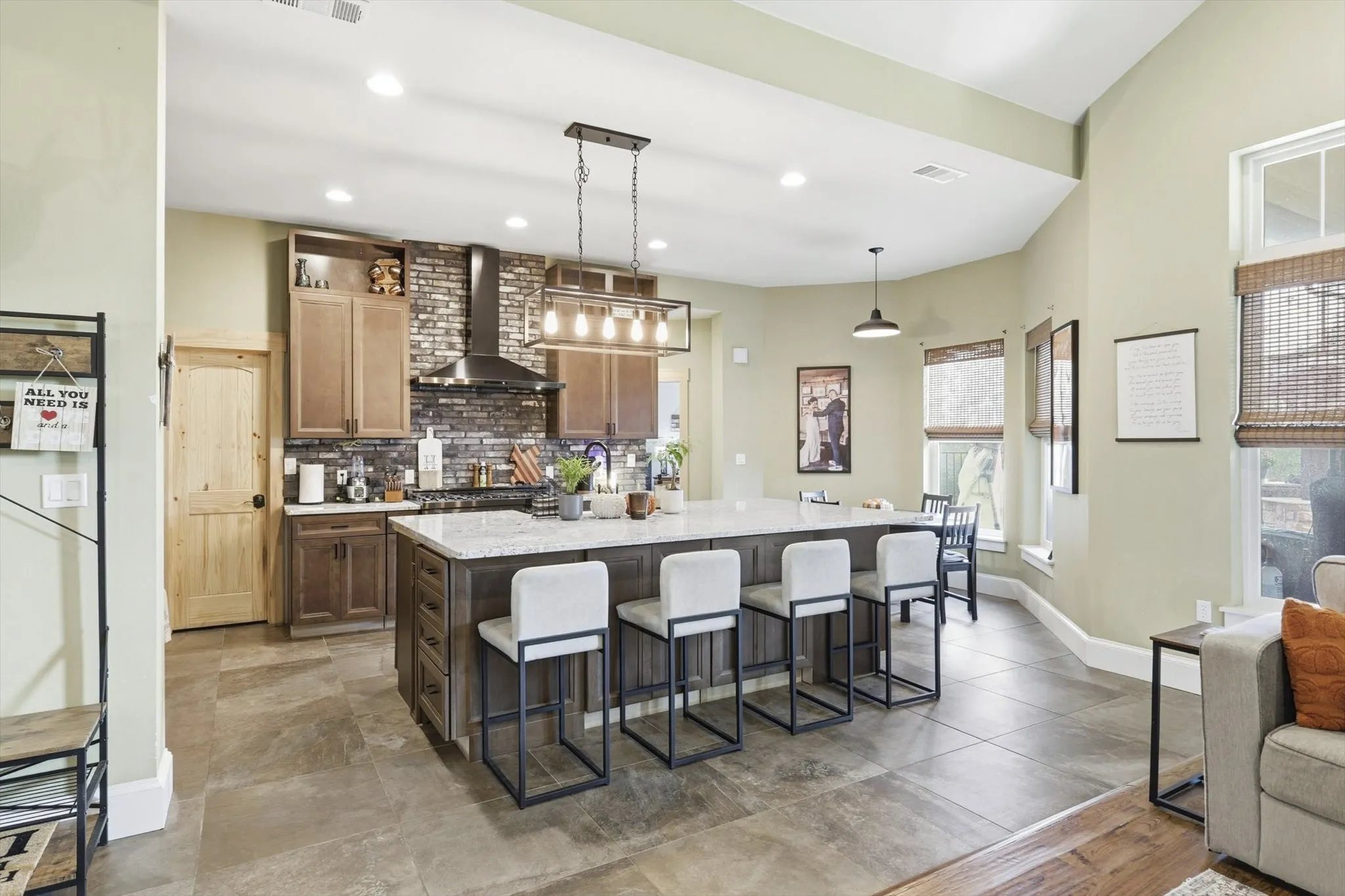 Kitchen with a breakfast bar area, decorative light fixtures, a kitchen island with sink, wall chimney exhaust hood, and decorative backsplash