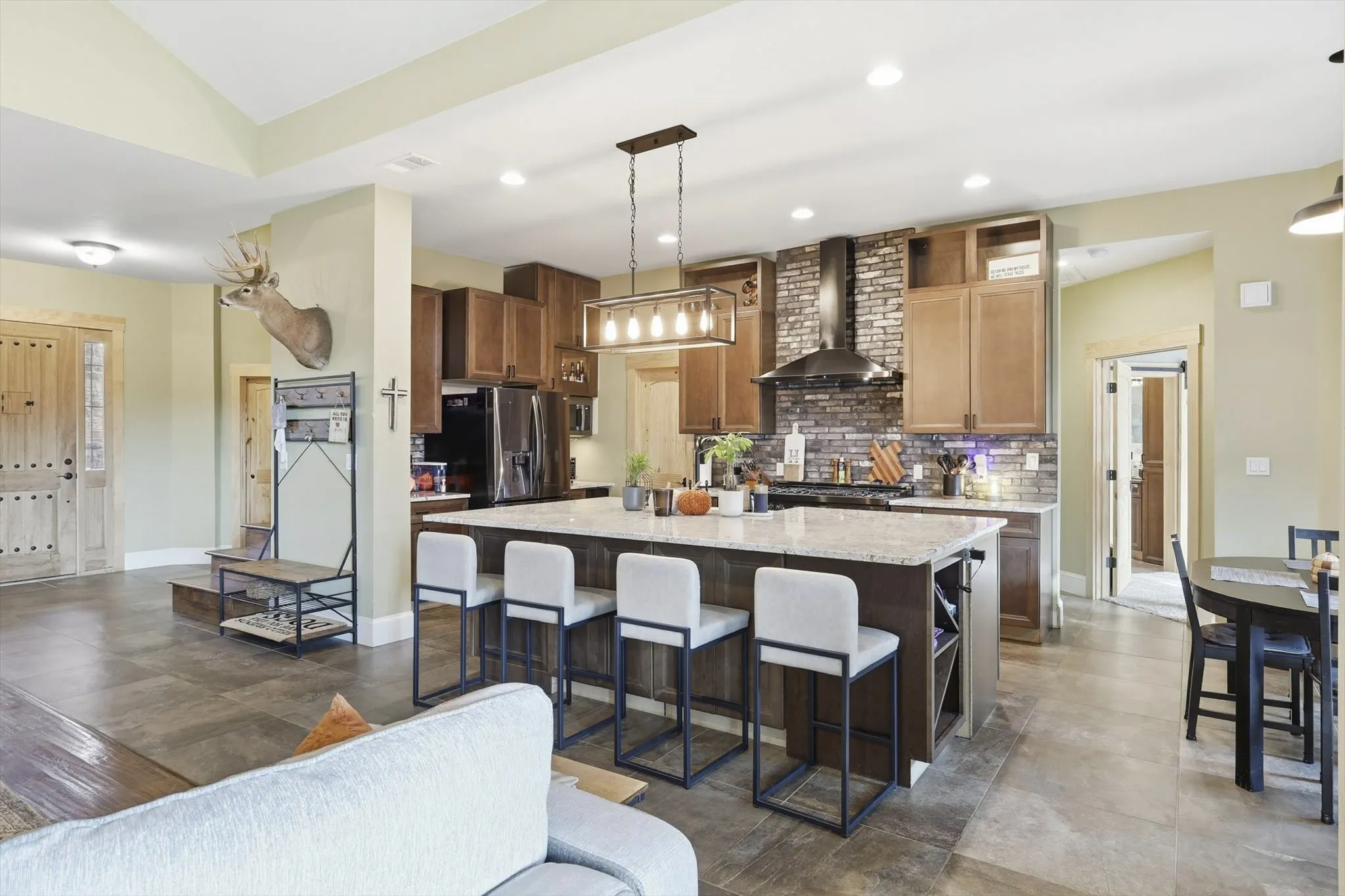 Kitchen with pendant lighting, light stone countertops, a kitchen breakfast bar, tasteful backsplash, and wall chimney range hood