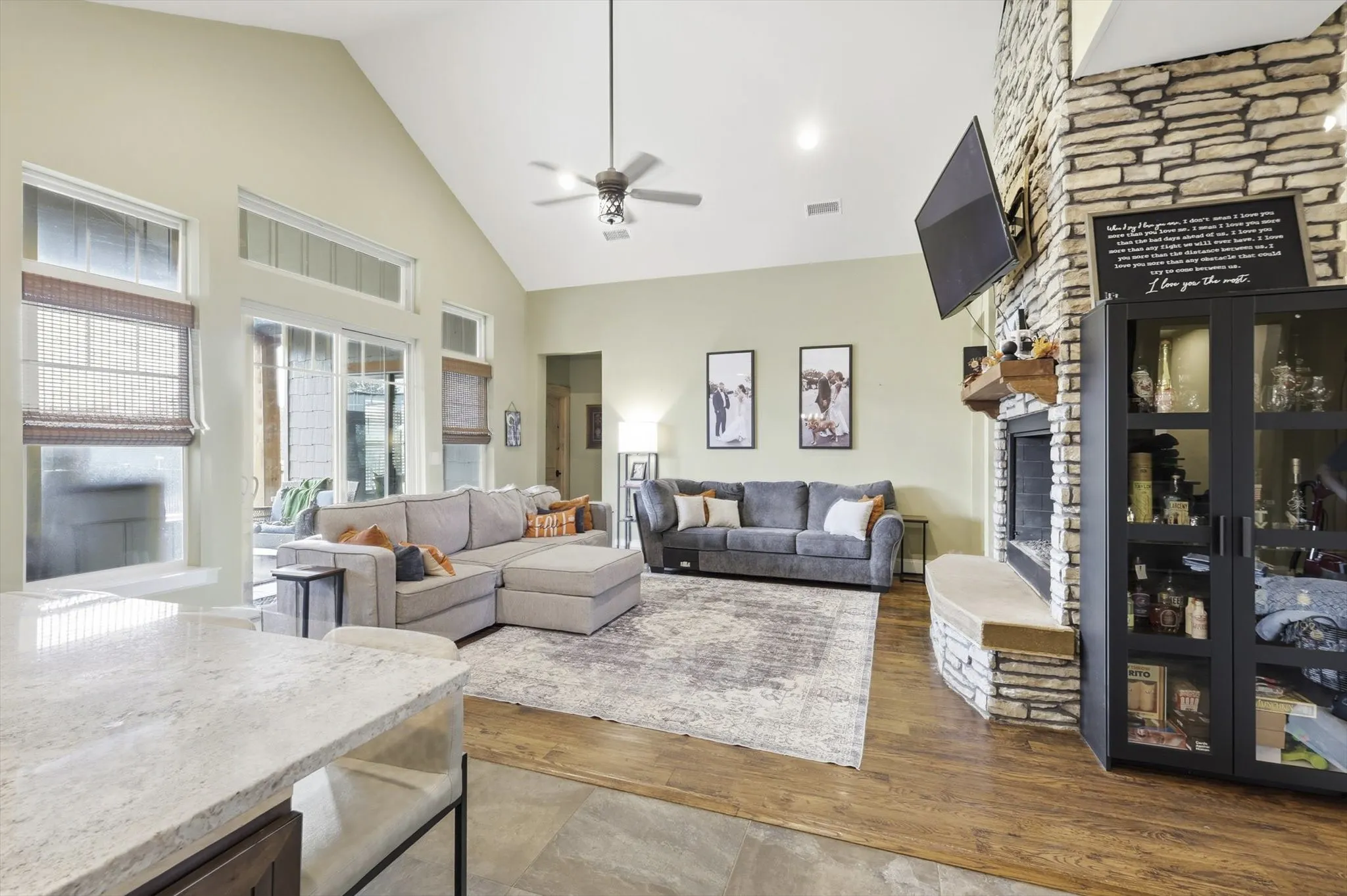 Living room with a fireplace, high vaulted ceiling, dark wood-style floors, ceiling fan, and recessed lighting