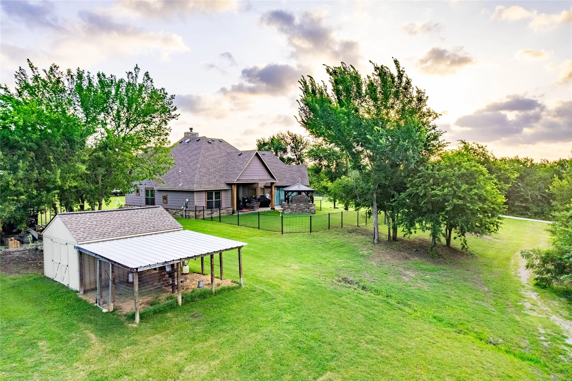 Expansive green lawn featuring a large detached shed with an attached covered lean-to, a fenced backyard, and mature trees