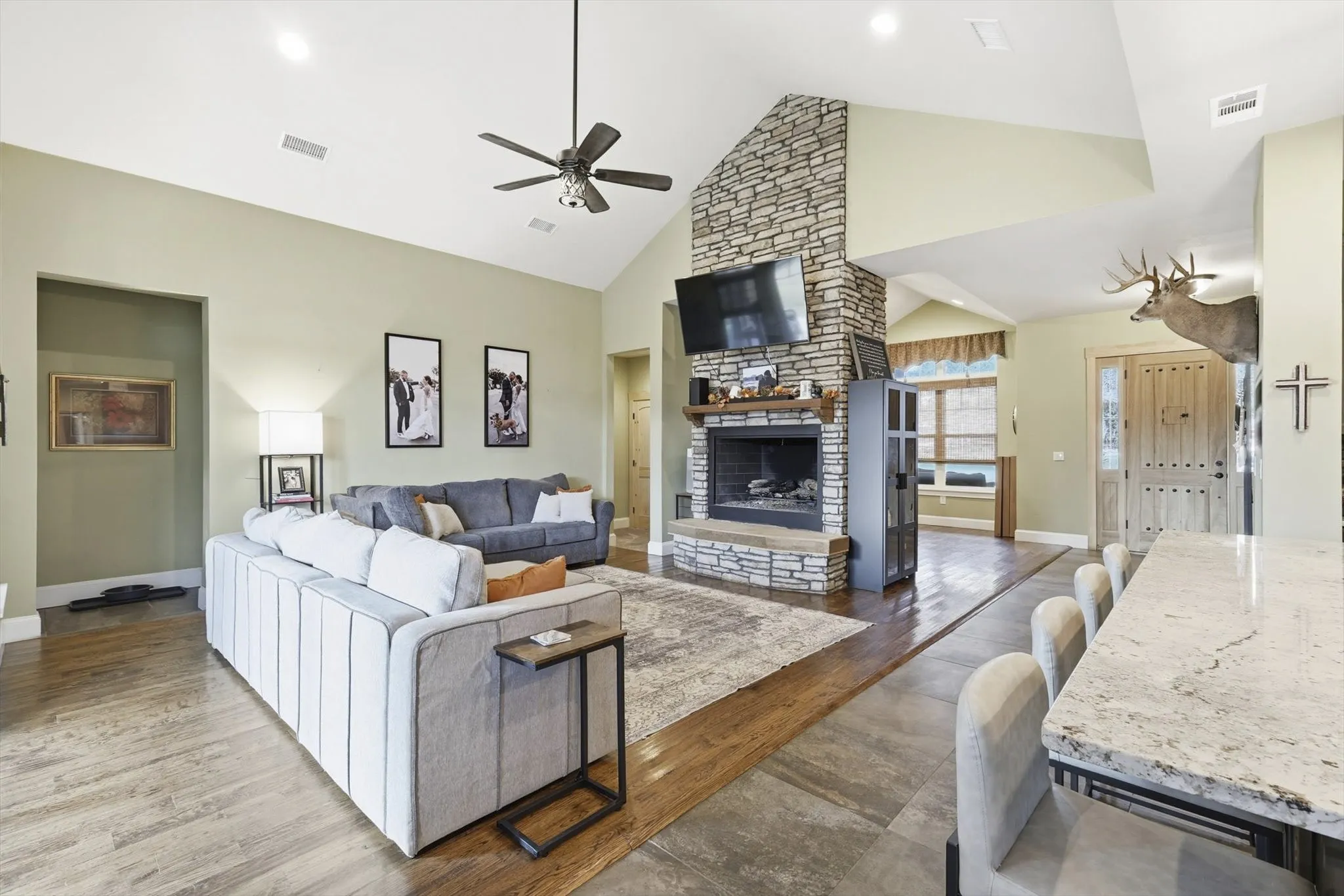 Living area featuring dark wood-style floors, high vaulted ceiling, a stone fireplace, and ceiling fan