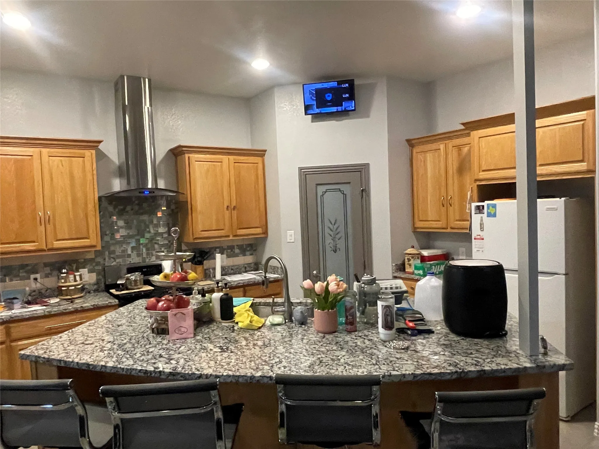 Kitchen featuring a kitchen breakfast bar, freestanding refrigerator, light stone countertops, brown cabinetry, and a center island with sink