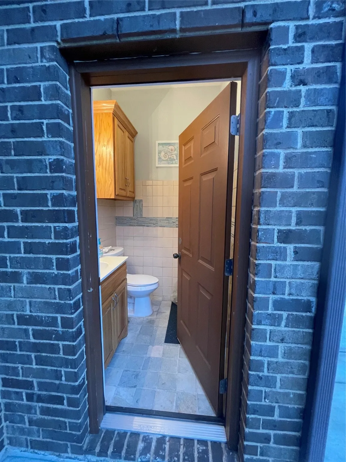 Half bathroom featuring vanity, tile walls, and brick wall