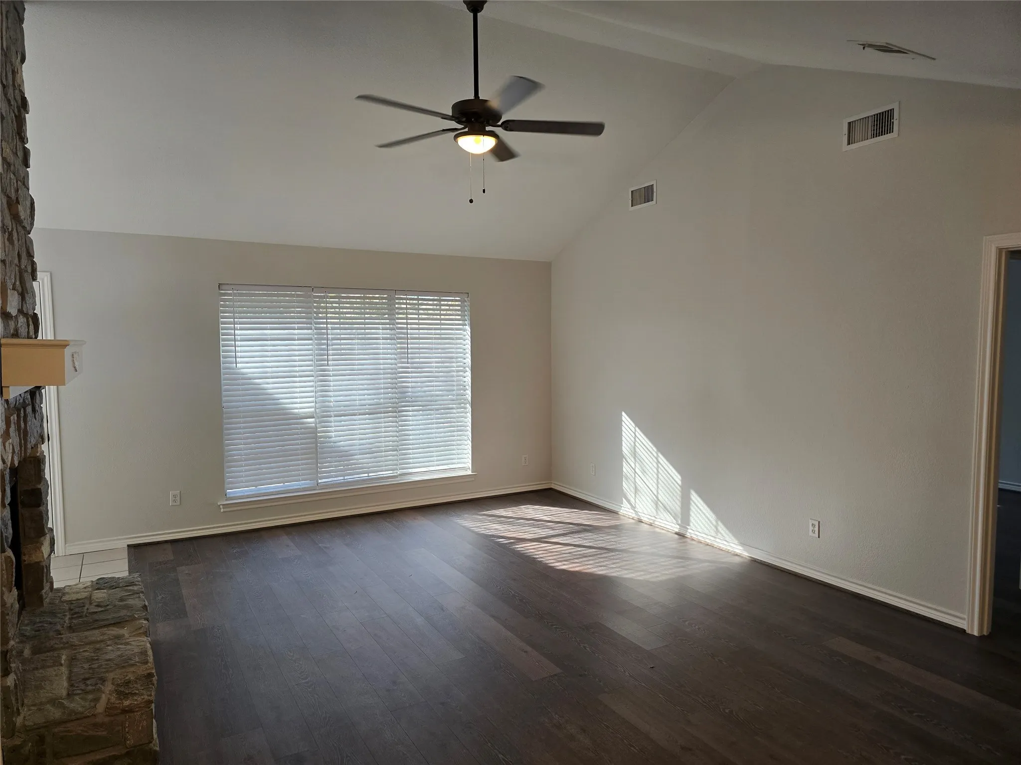 Living room featuring a stone fireplace, dark wood finished floors, a ceiling fan, and high vaulted ceiling