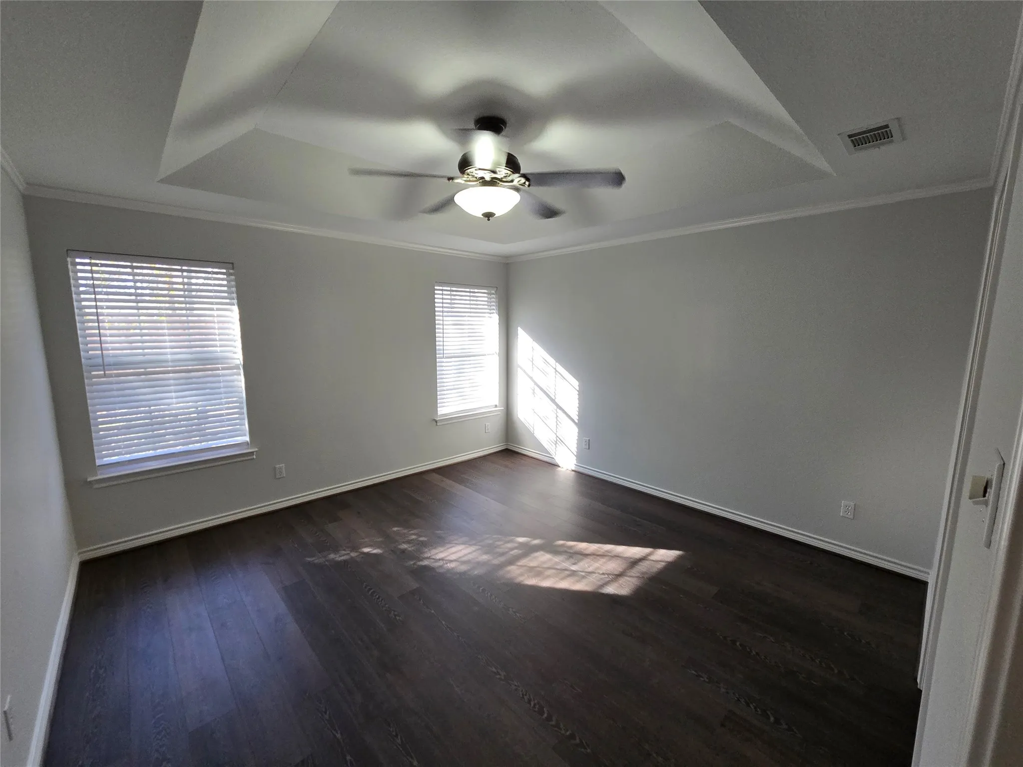Spare room with ornamental molding, a raised ceiling, dark wood-style floors, and ceiling fan