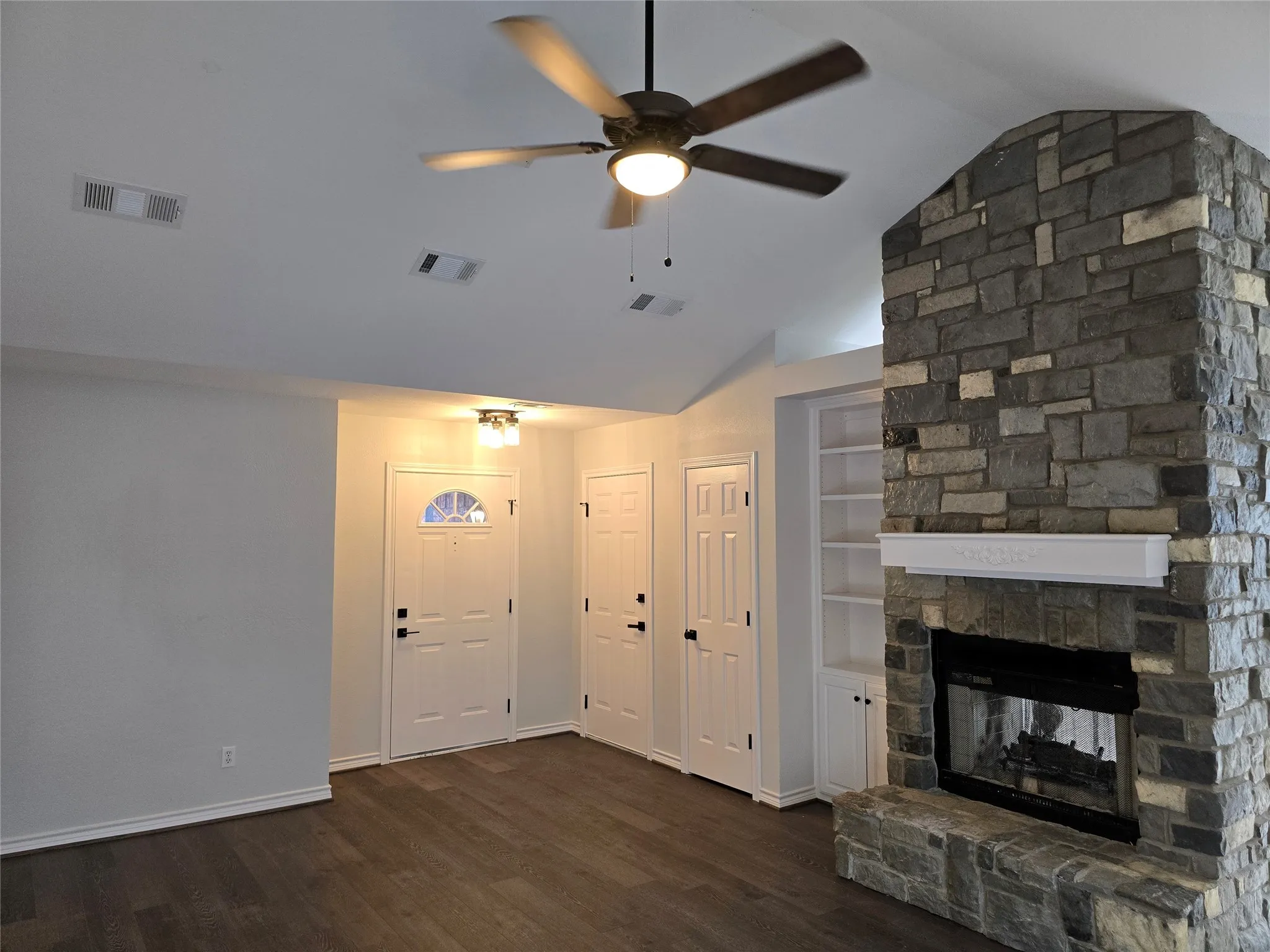 Living room featuring vaulted ceiling, a fireplace, dark wood-type flooring, built in shelves, and ceiling fan