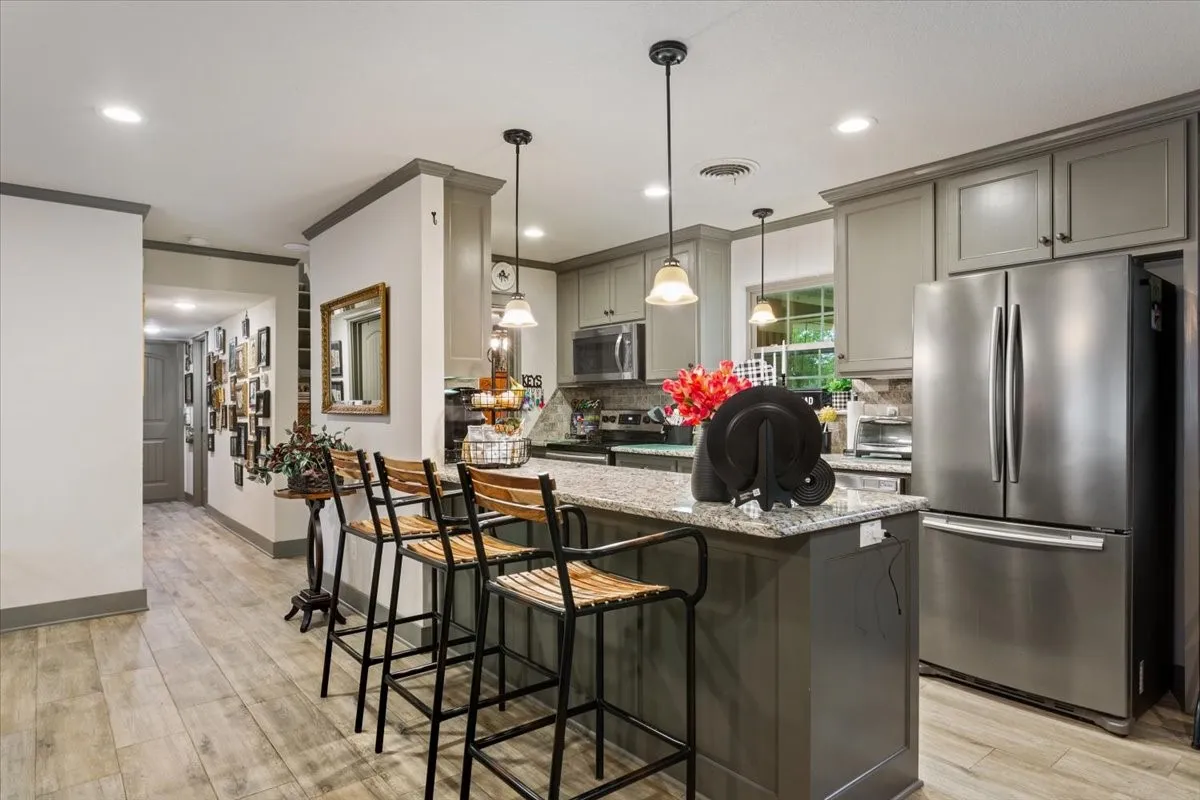 Kitchen featuring gray cabinetry, appliances with stainless steel finishes, light stone counters, a kitchen breakfast bar, and decorative light fixtures