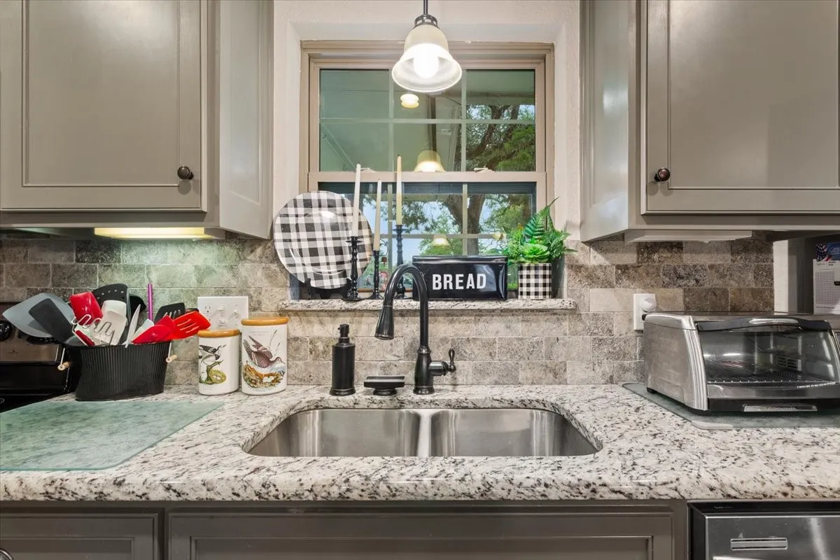 Kitchen featuring light stone counters, gray cabinetry, hanging light fixtures, and decorative backsplash