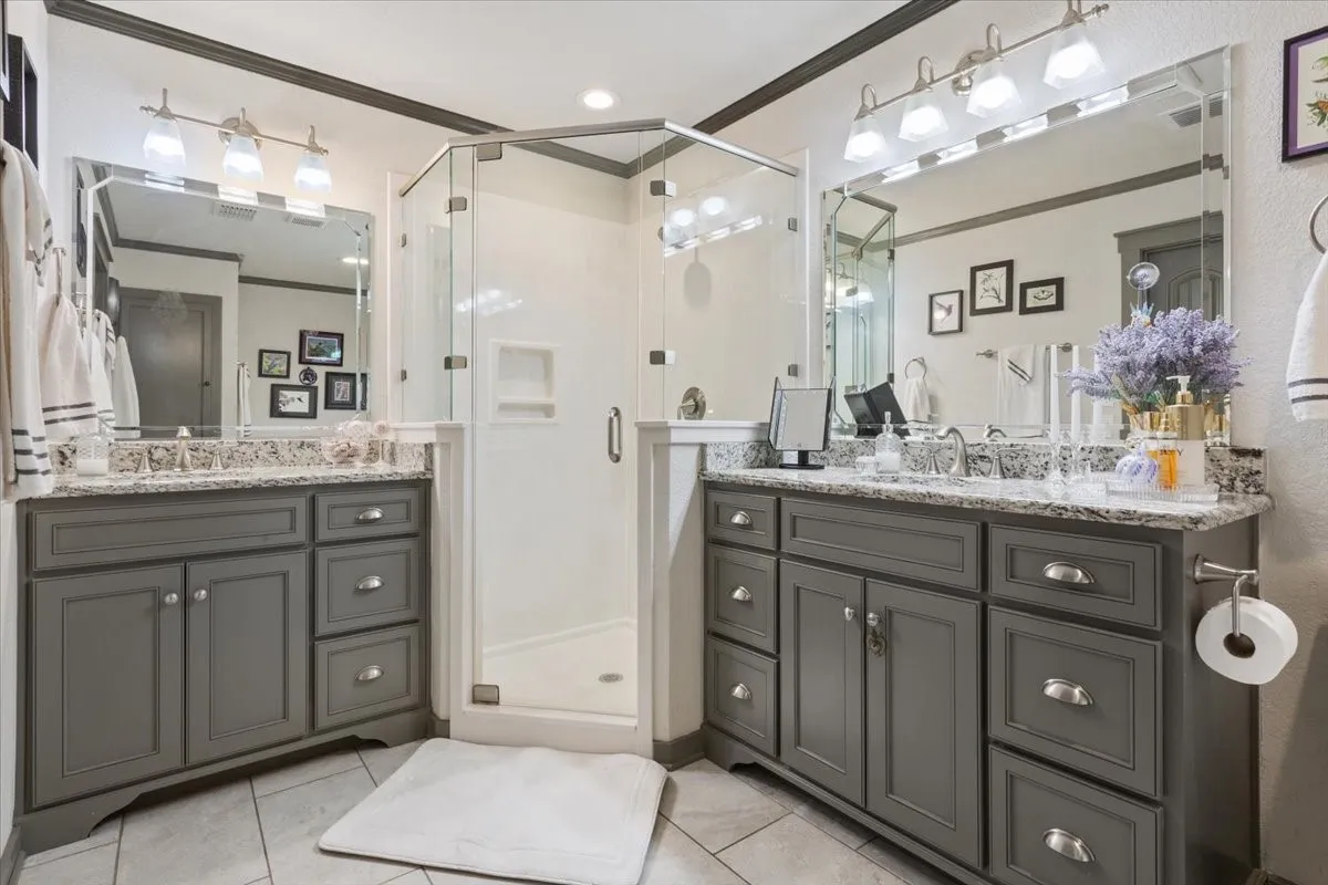 Bathroom with ornamental molding, a stall shower, light tile patterned floors, and two vanities